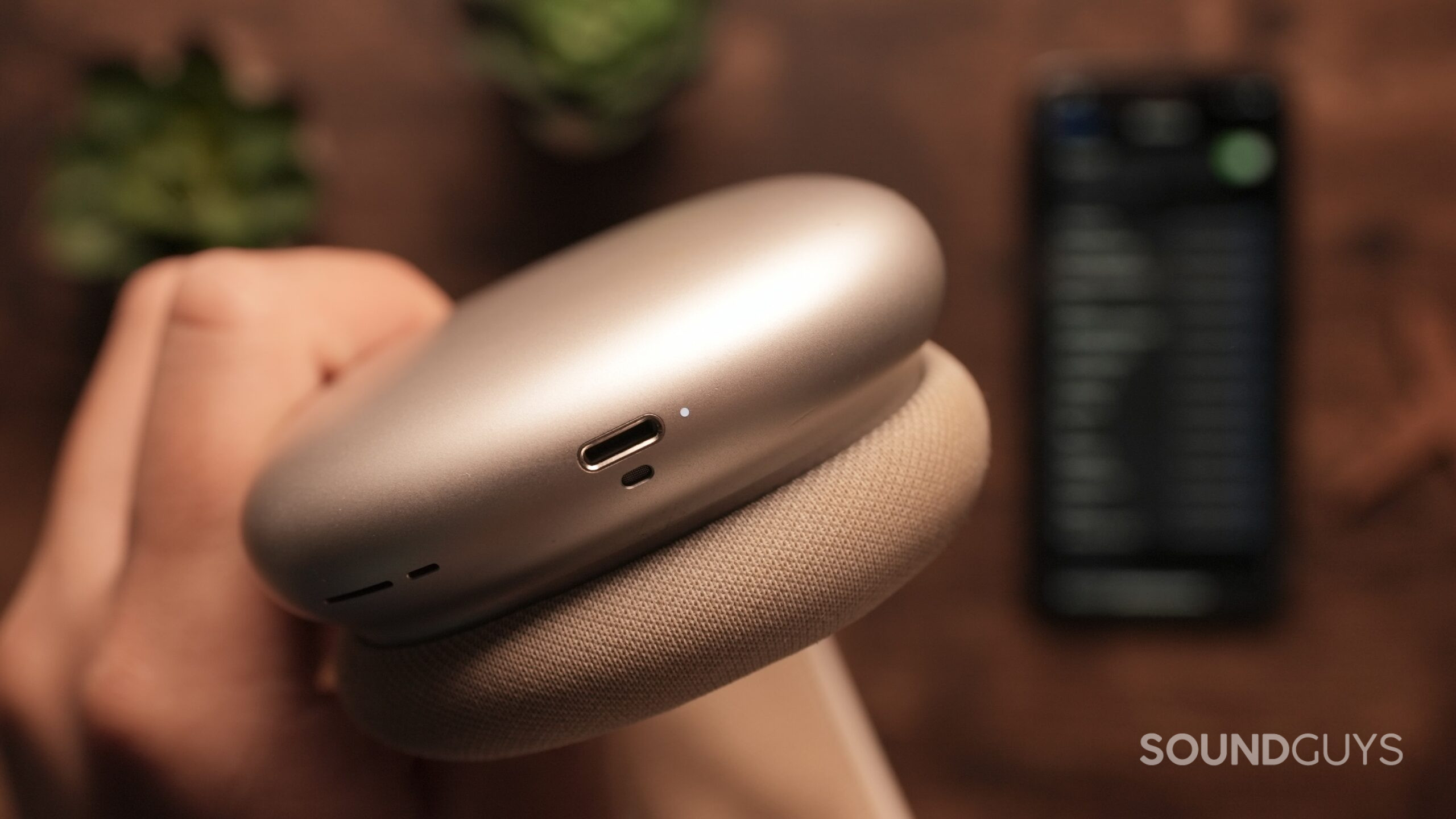A hand holds the Airpods Max, showing the flashing light.