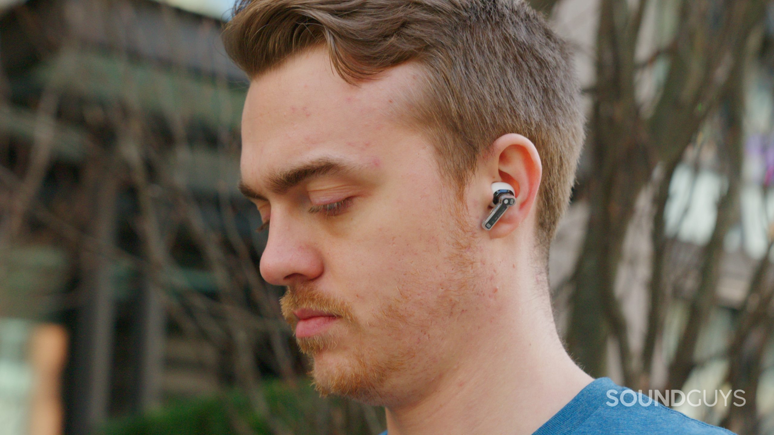 A man faces left and looks down while wearing the Nothing Ear (2) outdoors.