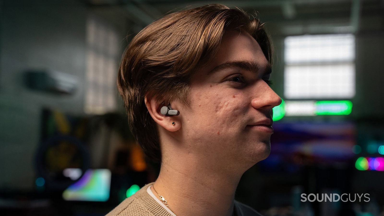 A man wearing the Audio-Technica ATH-TWX7 earbuds facing right in a dark room.