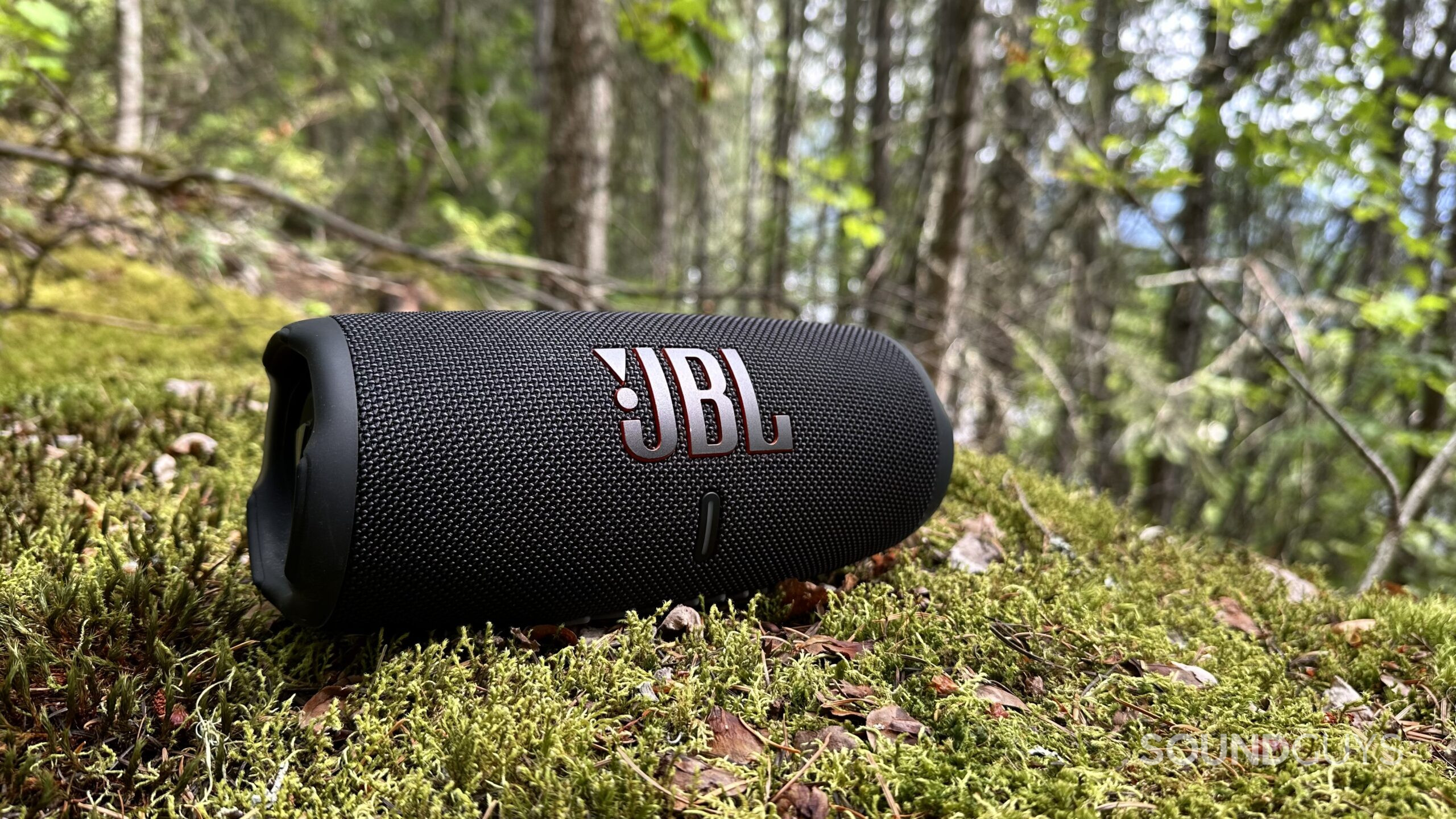 JBL Charge 5 speaker placed on some mossy rocks, slightly angled in a forest.