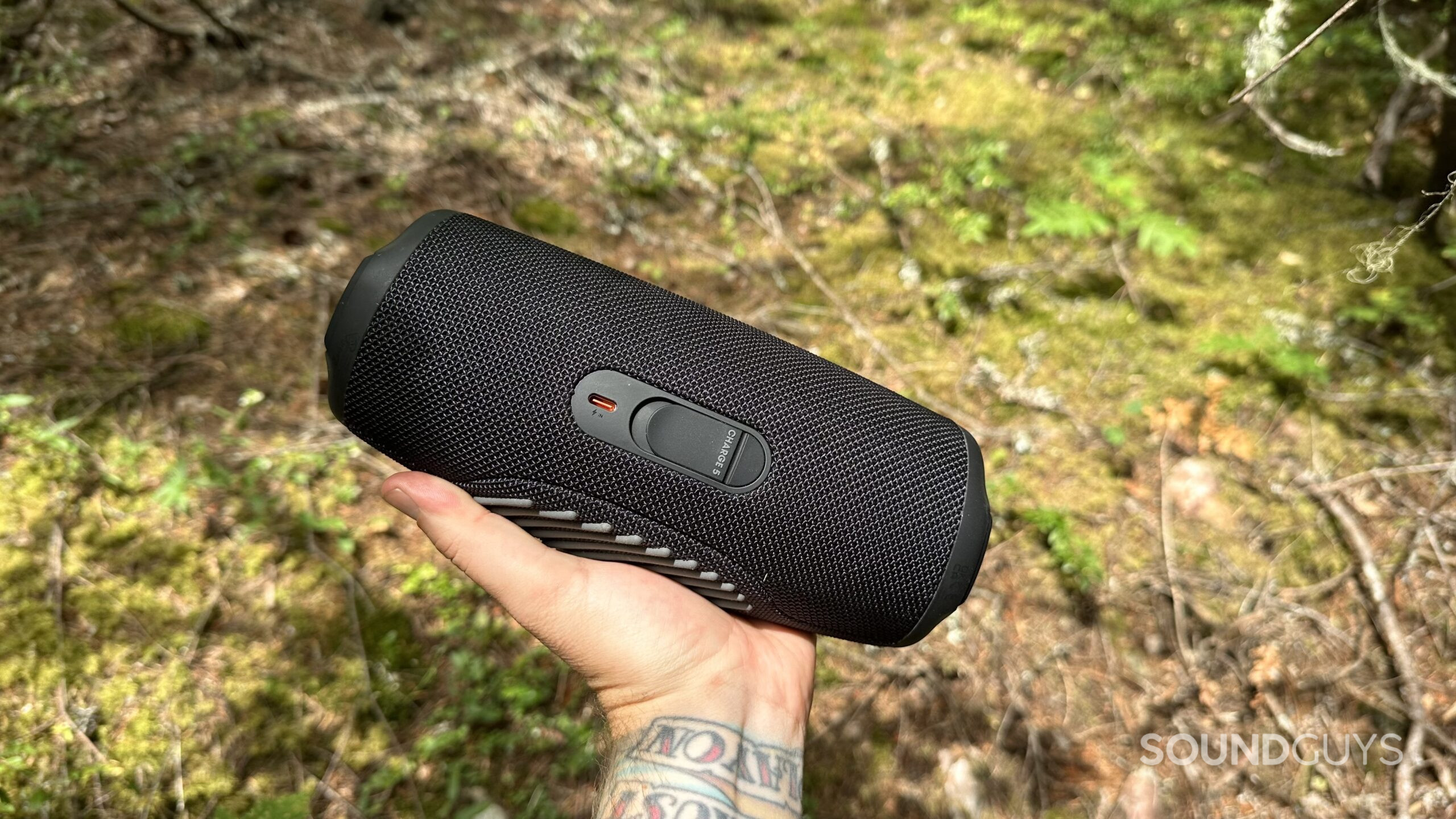 JBL Charge 5 speaker in hand, showing its USB-C connection port.