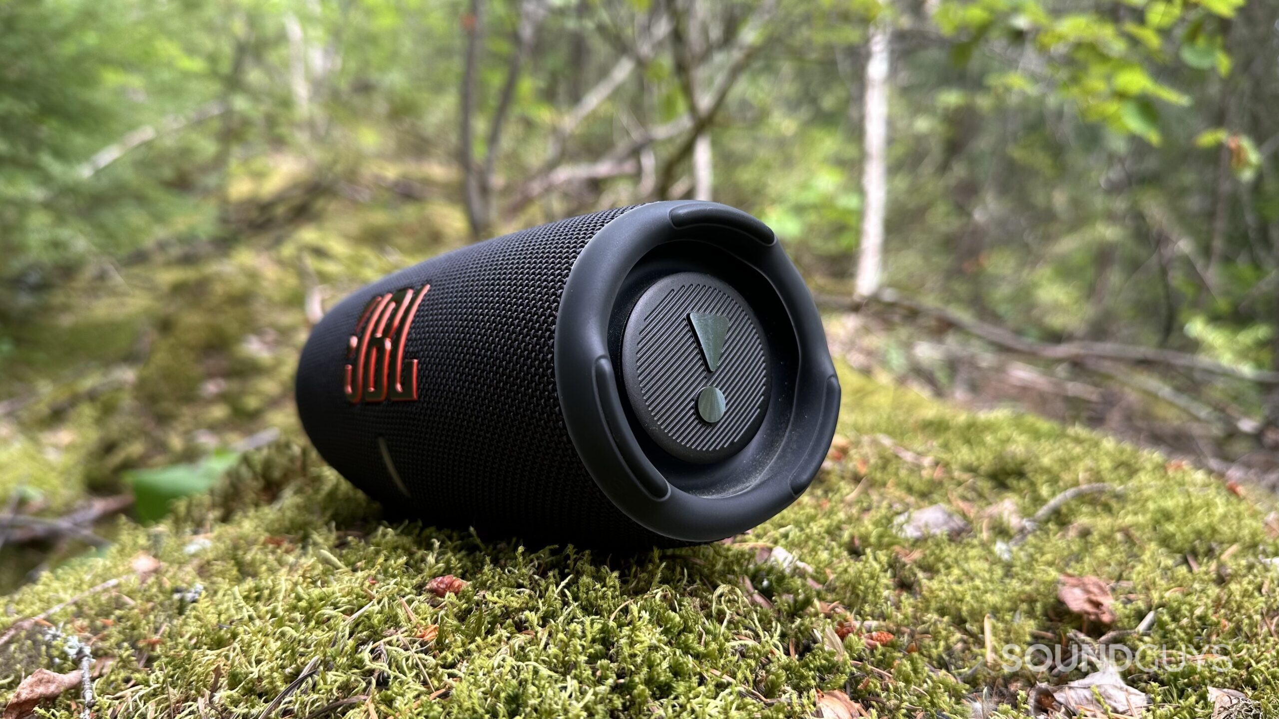 JBL Charge 5 speaker placed on some mossy rocks in a forest, showing its passive radiators.