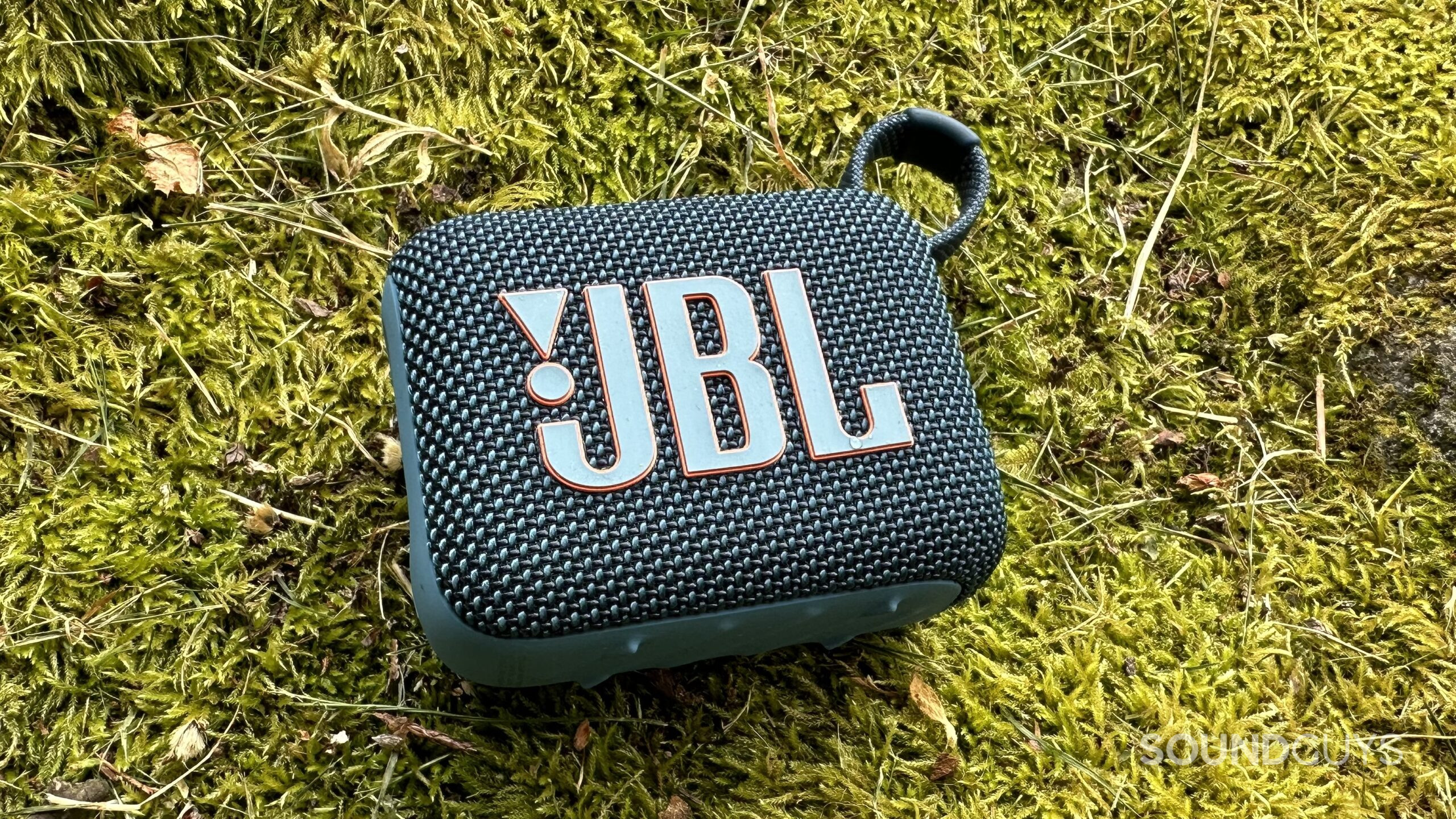 A JBL Go 4 speaker placed on some moss.