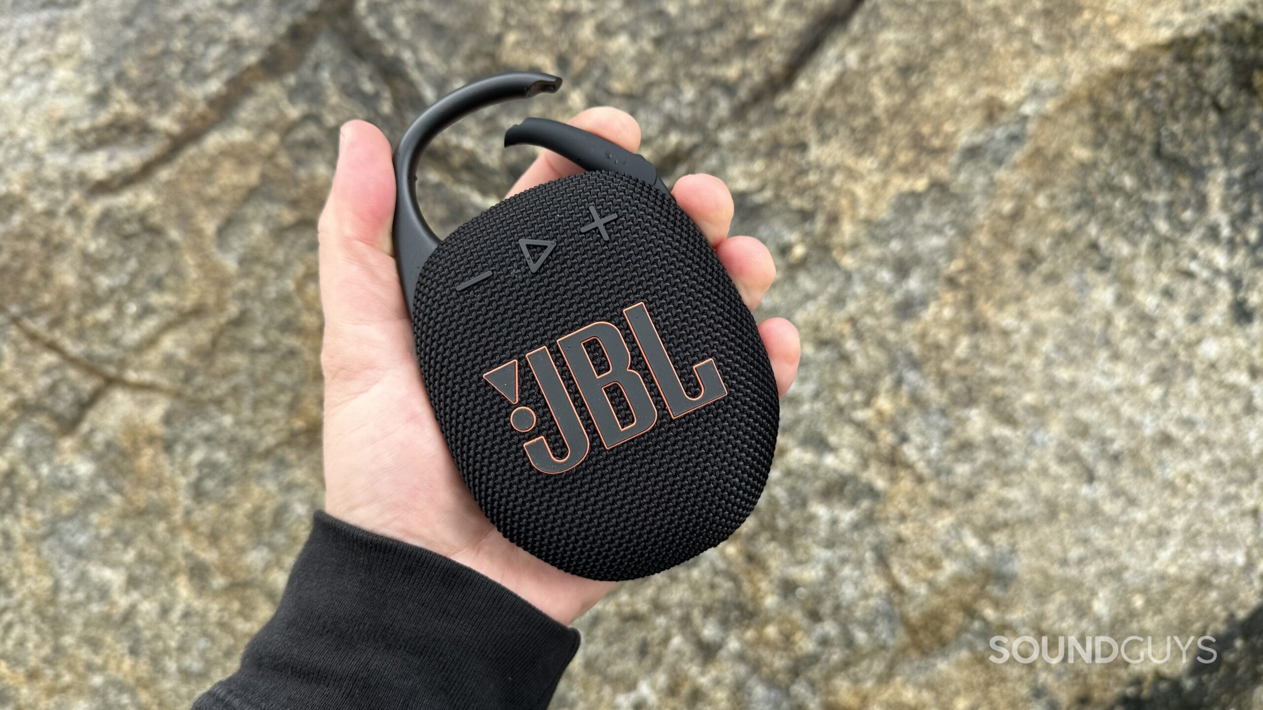 A JBL Clip 5 in hand holding the carabiner clip open.