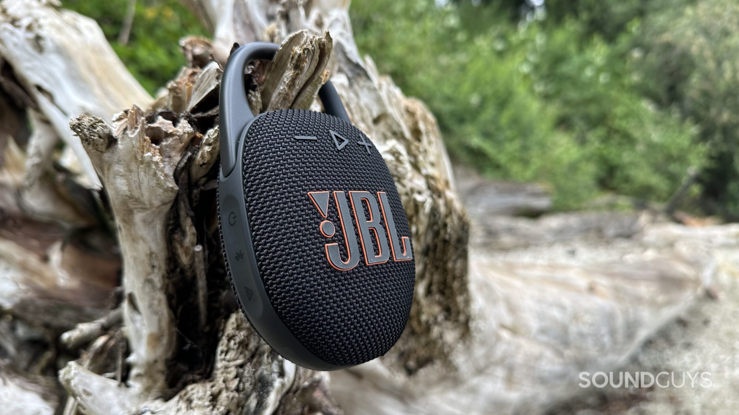 A JBL Clip 5 hanging off a large piece of driftwood.
