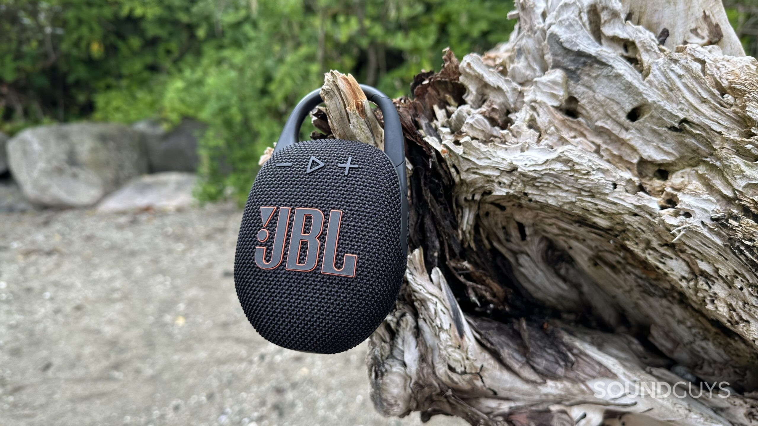 A JBL Clip 5 hanging off a large piece of driftwood.