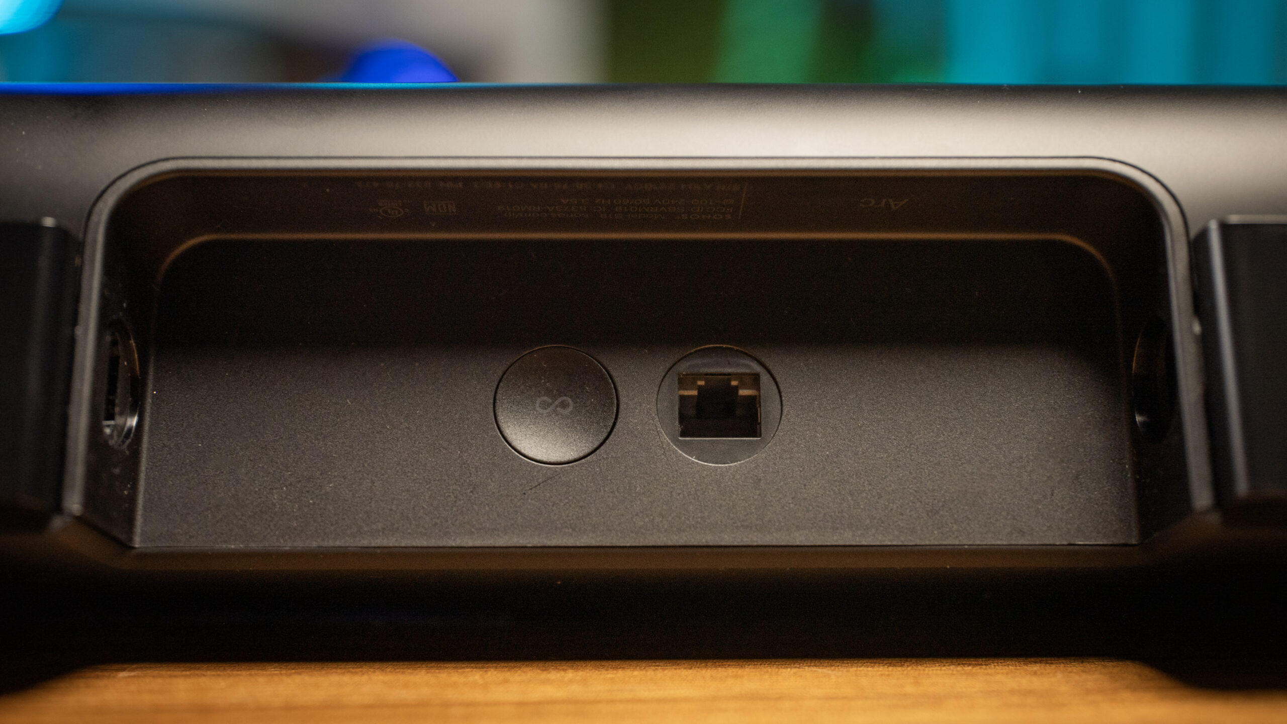 Close-up of the ethernet port and connection button on the back of the Sonos Arc soundbar placed on top of a wooden table.