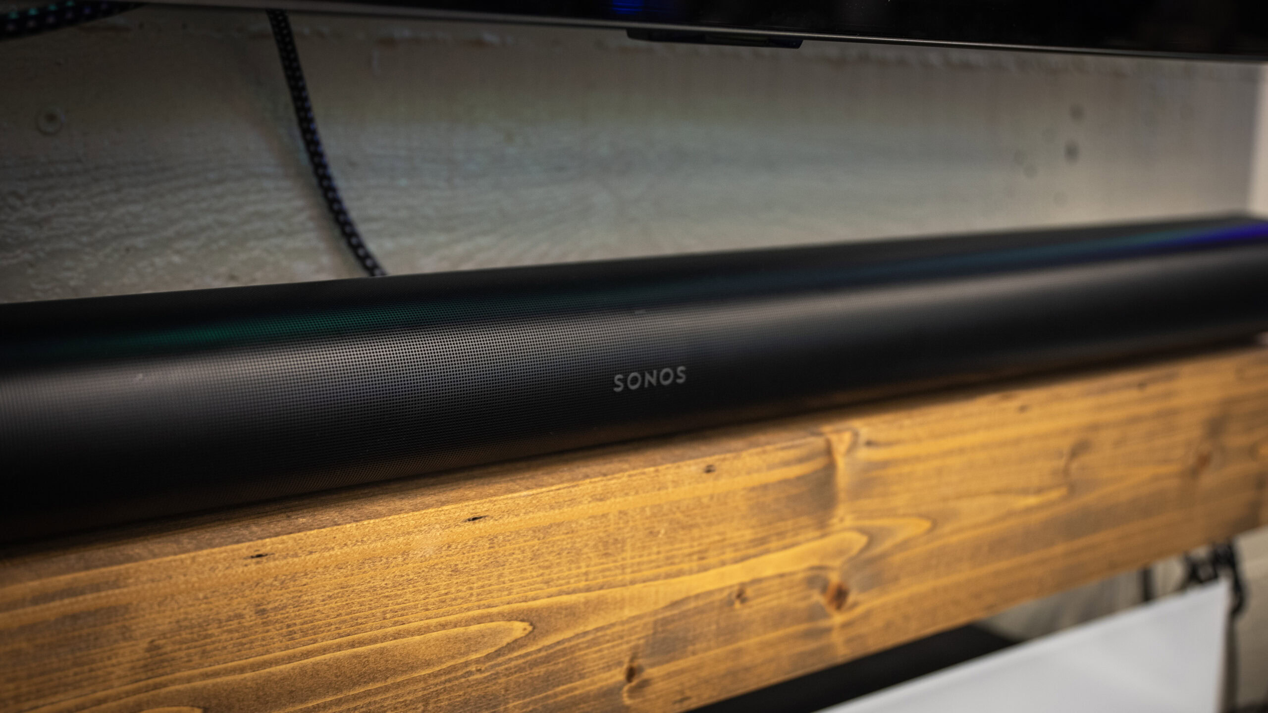 A semi-side profile shot of the Sonos Arc sound bar on top of a soundbar table underneath a flat screen TV.