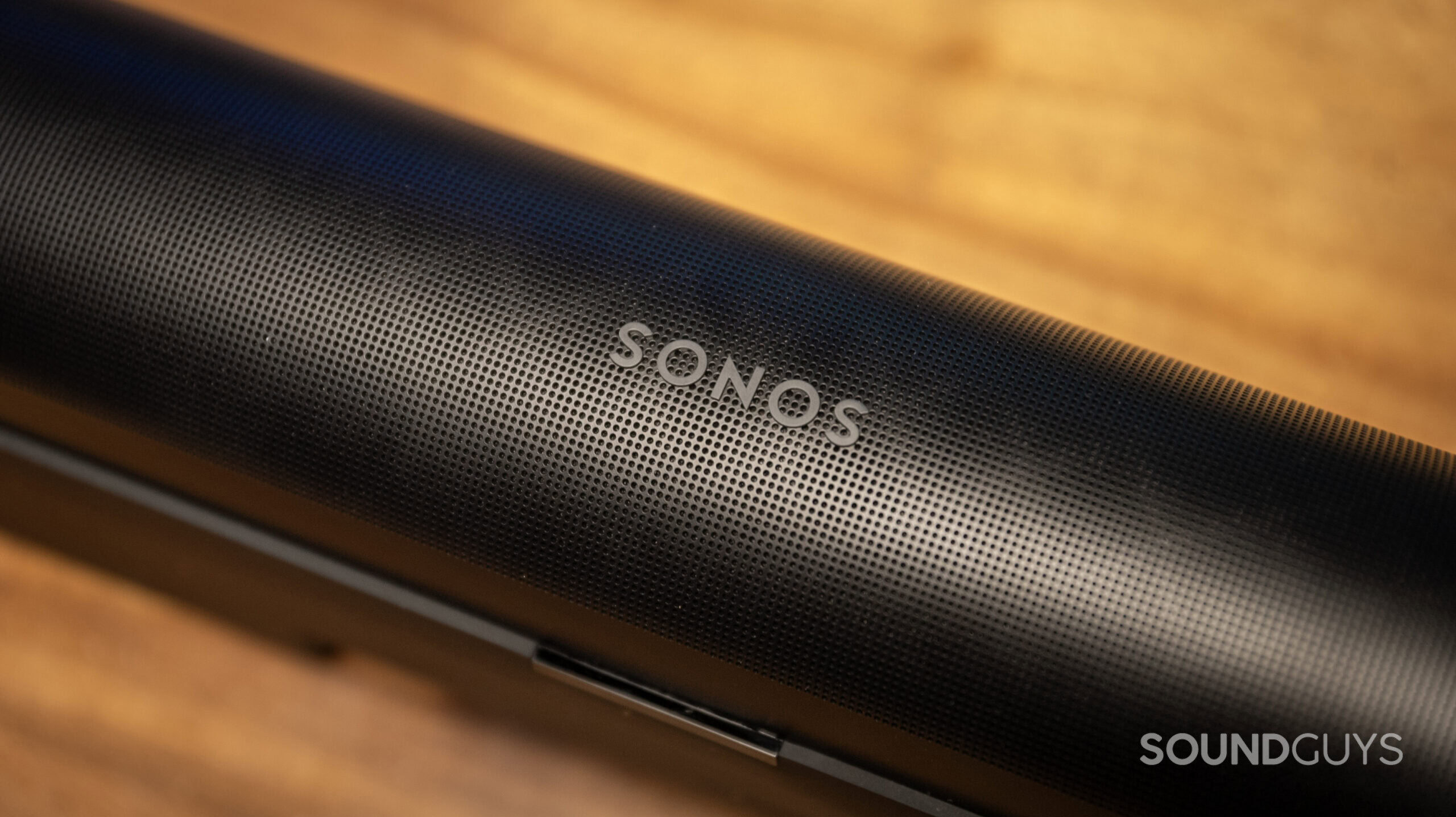 Close up of the Sonos logo on the Sonos Arc soundbar that sits on top of a wooden table.