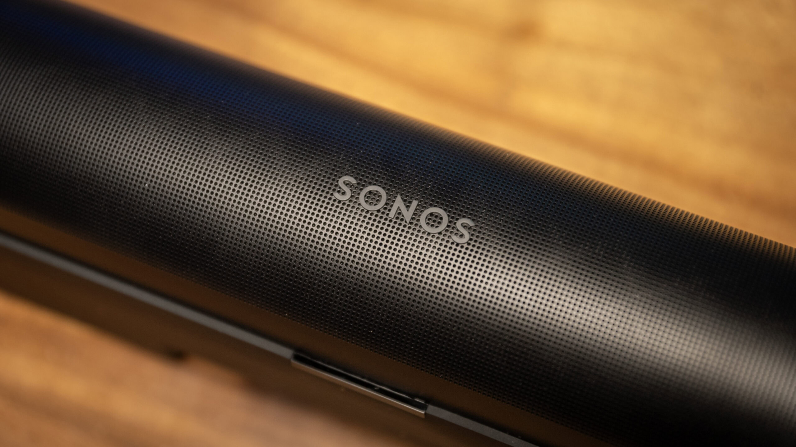 Close up of the Sonos logo on the Sonos Arc soundbar that sits on top of a wooden table.