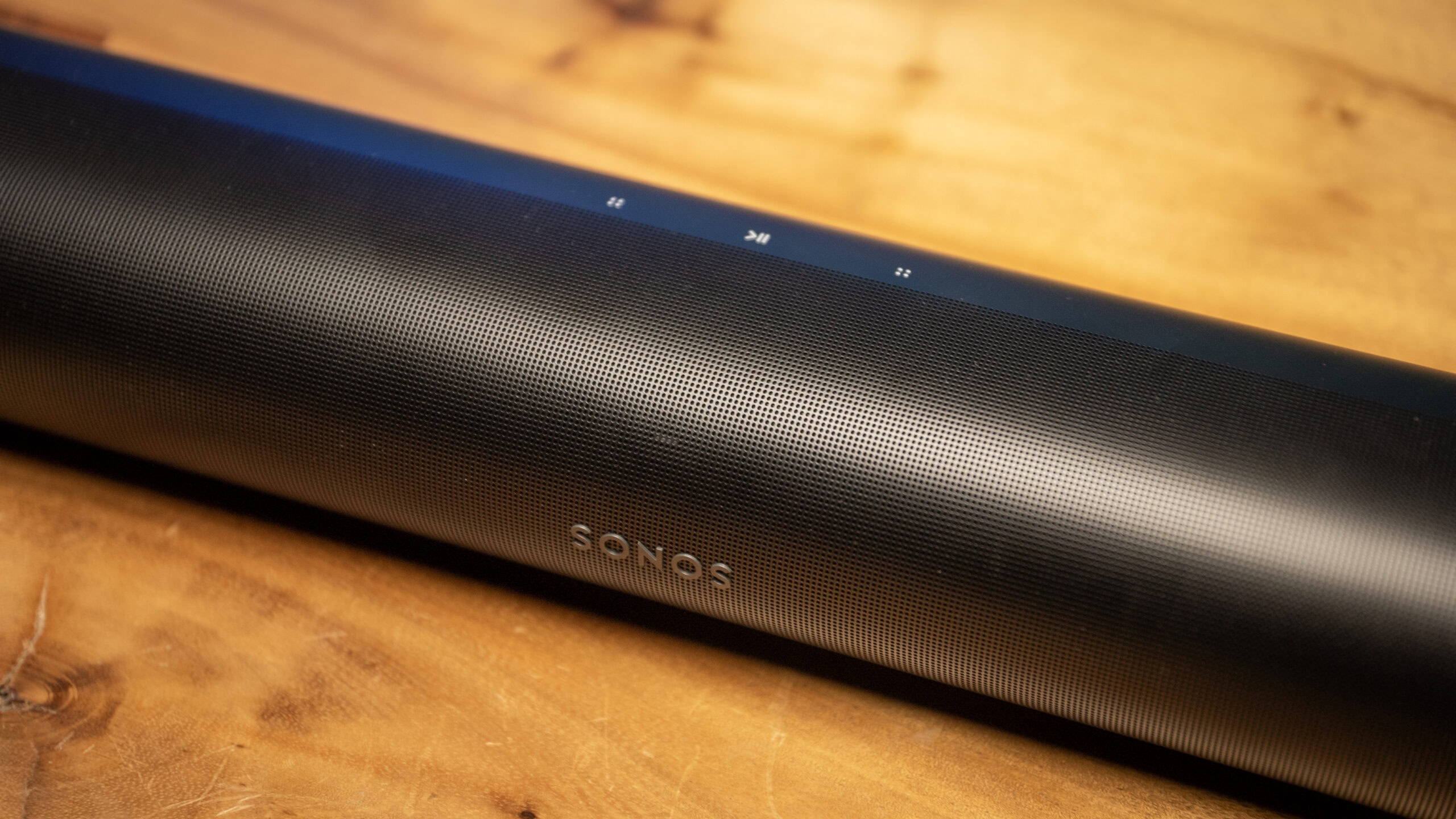 Top-down angle looking at the control buttons and logo for the Sonos Arc soundbar placed on a wooden table.