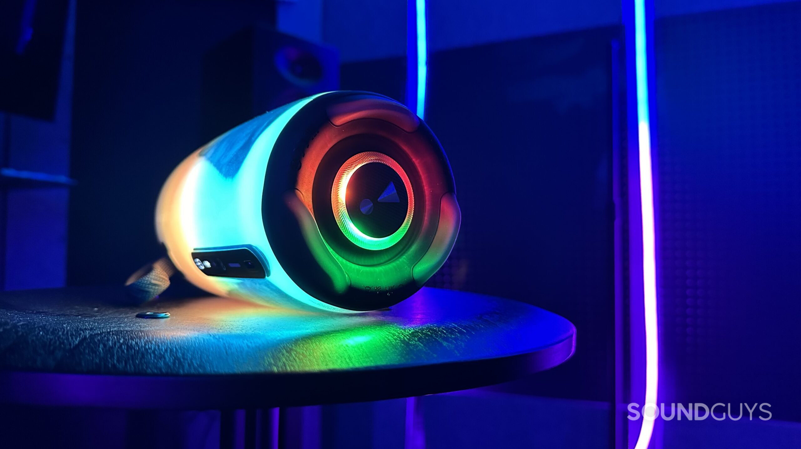 A lit up JBL Pulse 5 on its side in a cool looking room, showing its passive radiator.