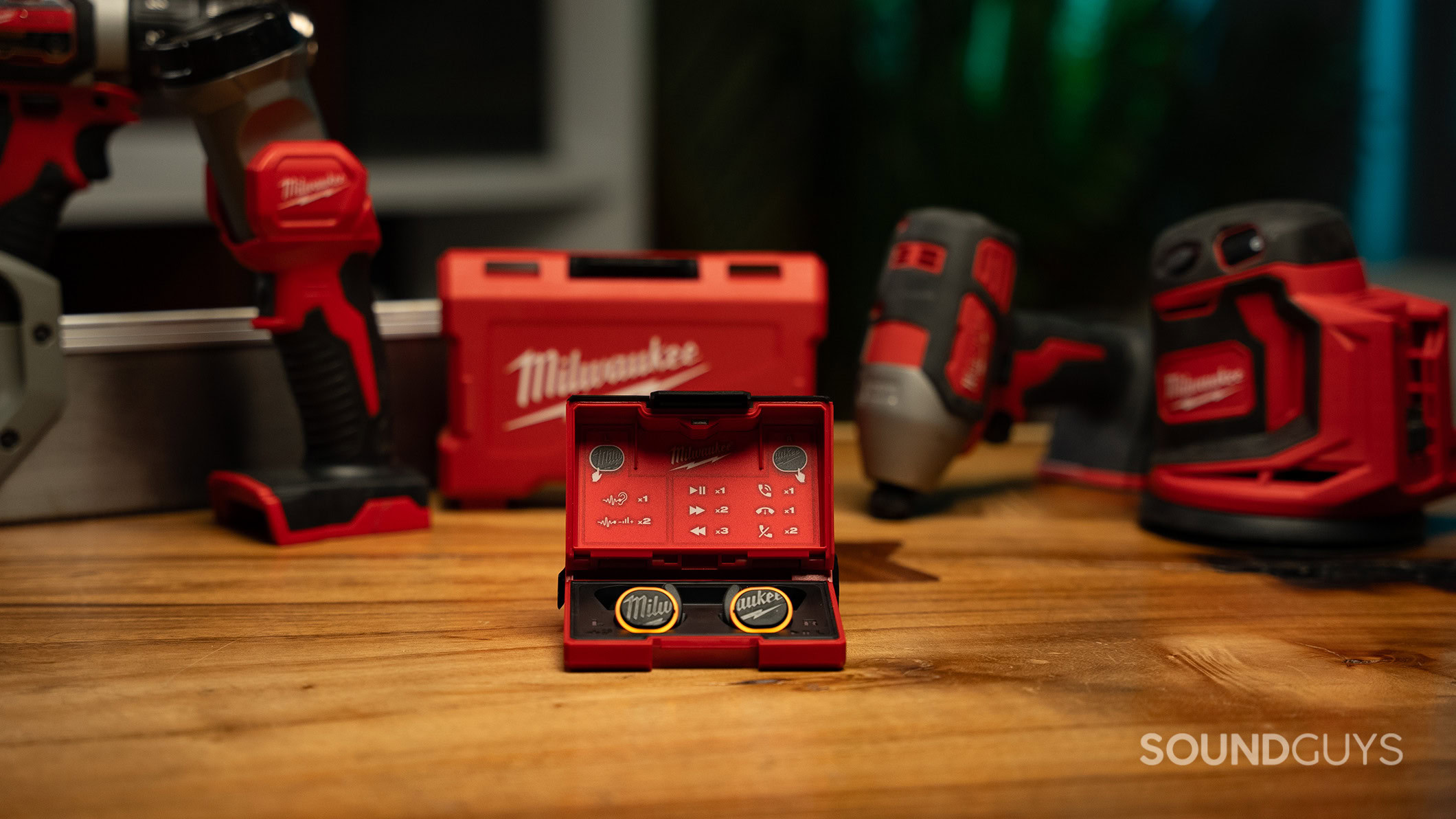 The Milwaukee REDLITHIUM Jobsite Earbuds in front of some Milwaukee power tools on a table. 