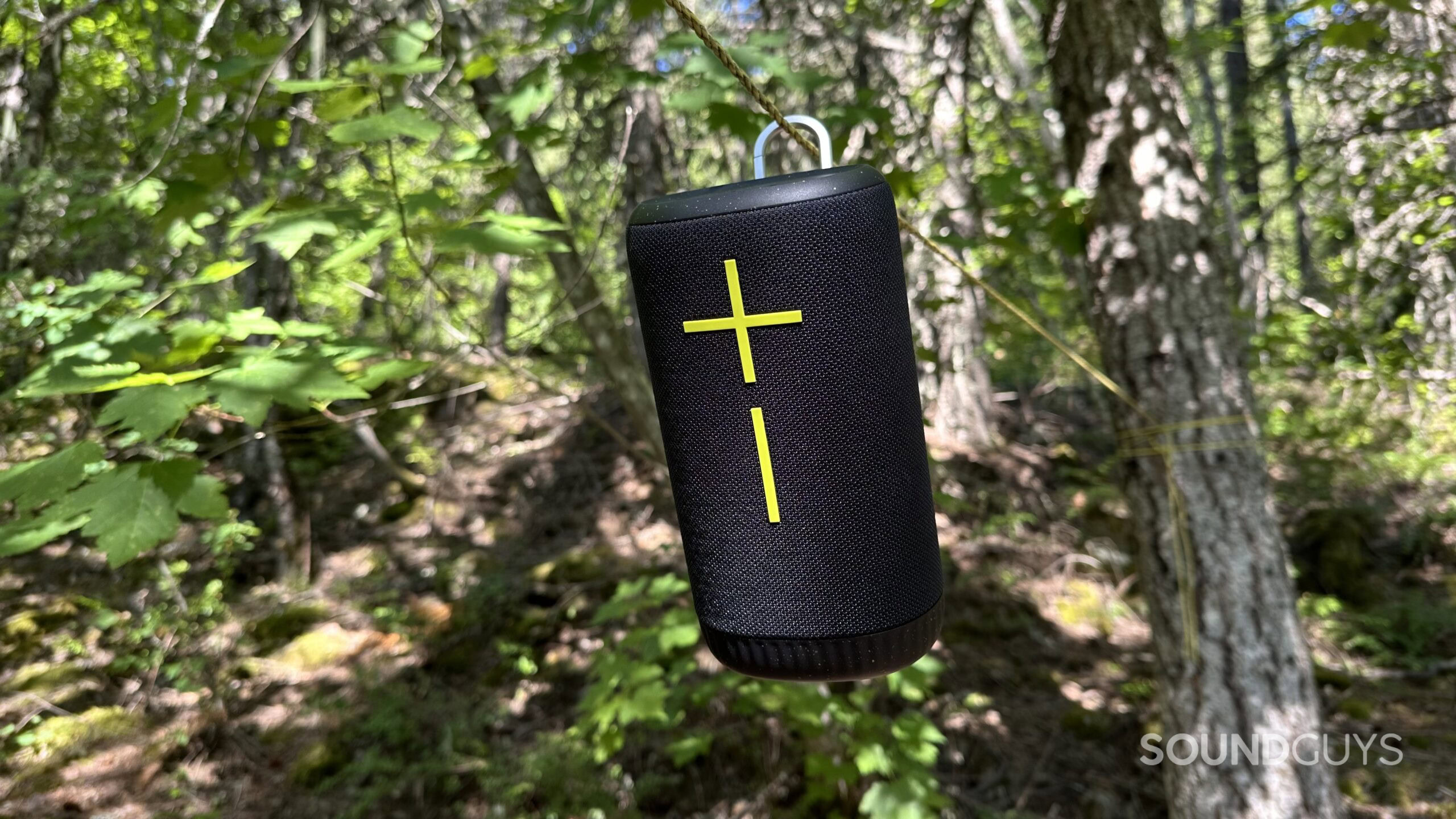 A Ultimate Ears Everboom boom speaker clipped to a rope in a forest.