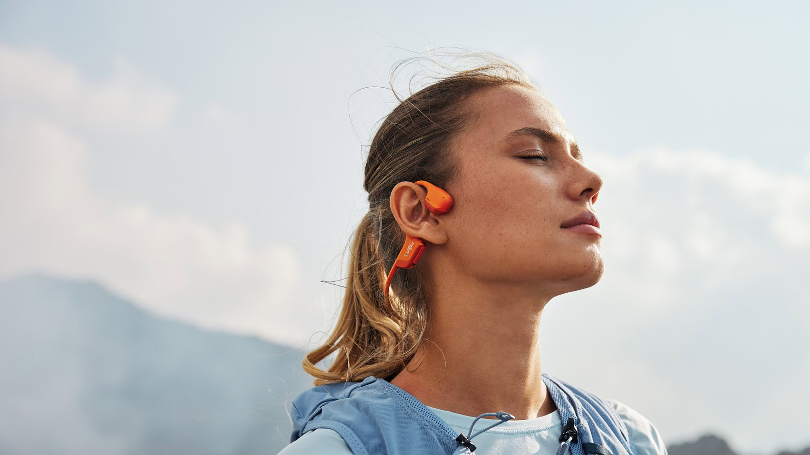 a woman wearing the shokz openrun pro 2 in orange