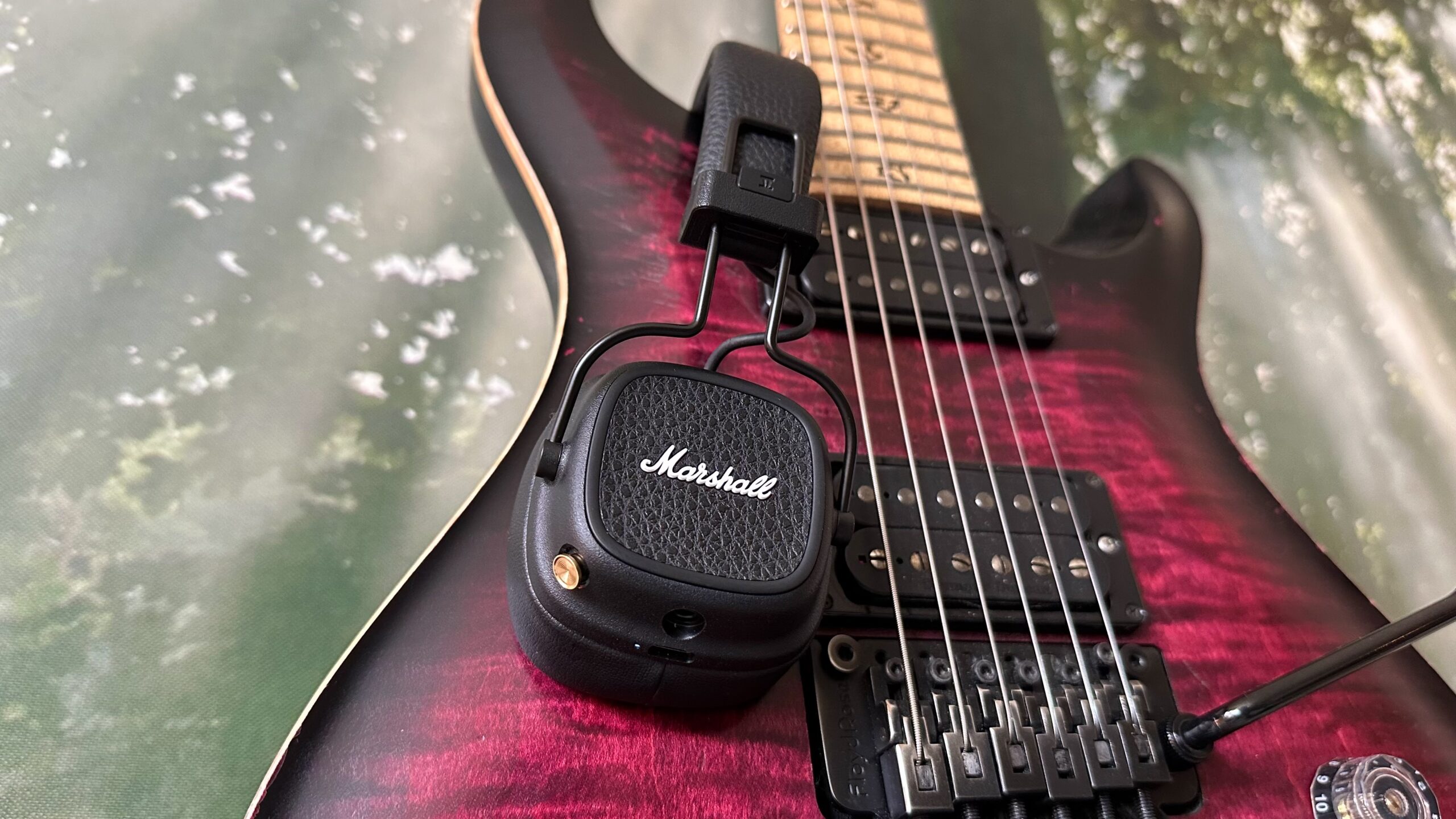 A pair of Marshall Major V headphones resting on a guitar with a forest back ground.