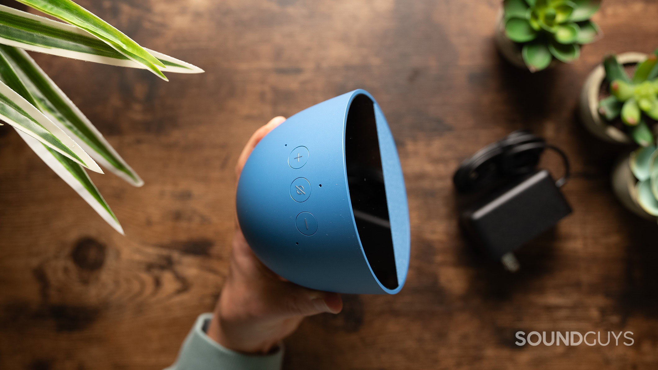 A hand holds the Amazon Echo Spot (2024) showing the controls on top of the speaker. 