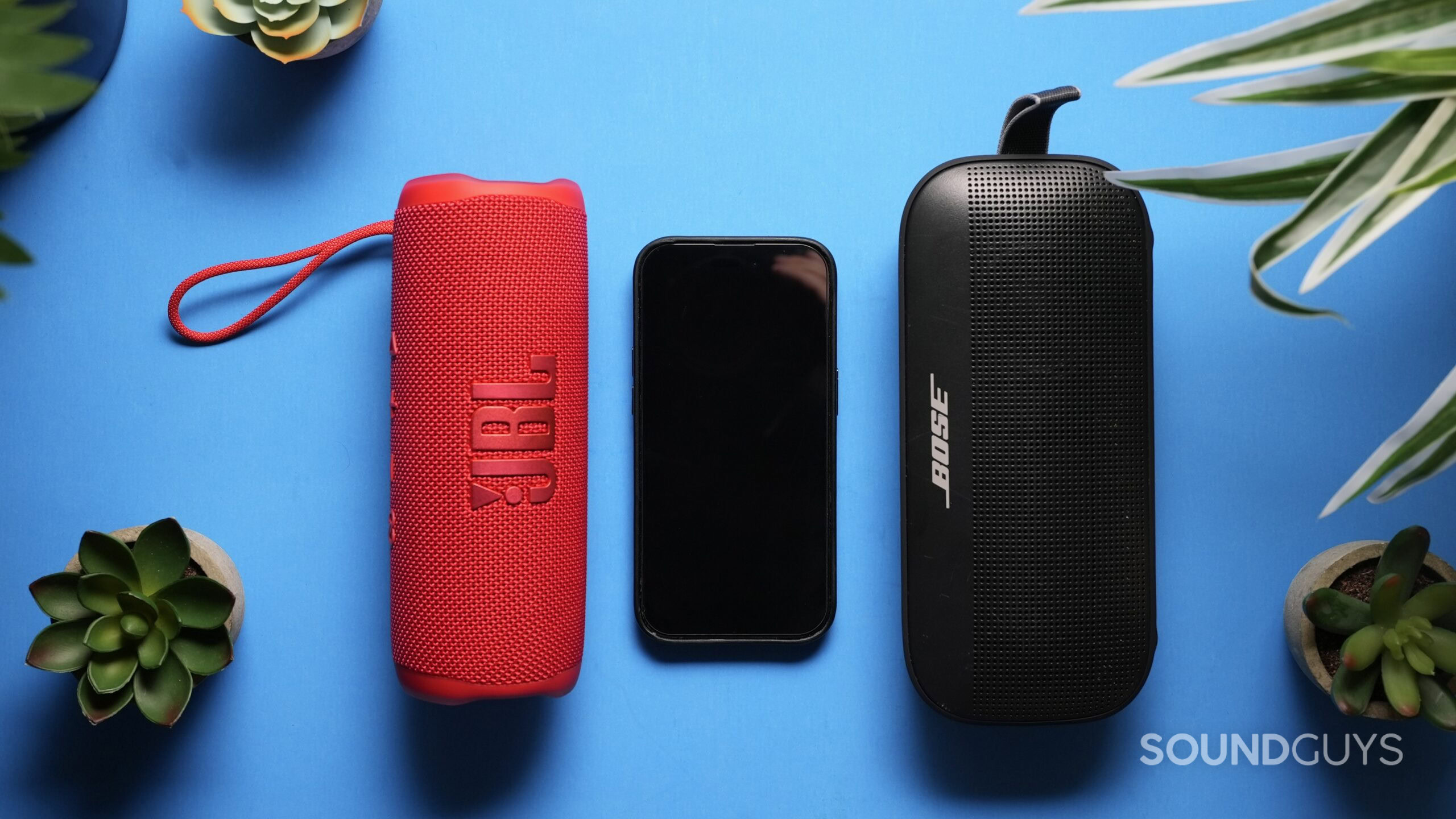 Photo of a JBL Flip 6 and Bose Soundlink Flex with an iPhone 14 Pro in the middle showing size difference