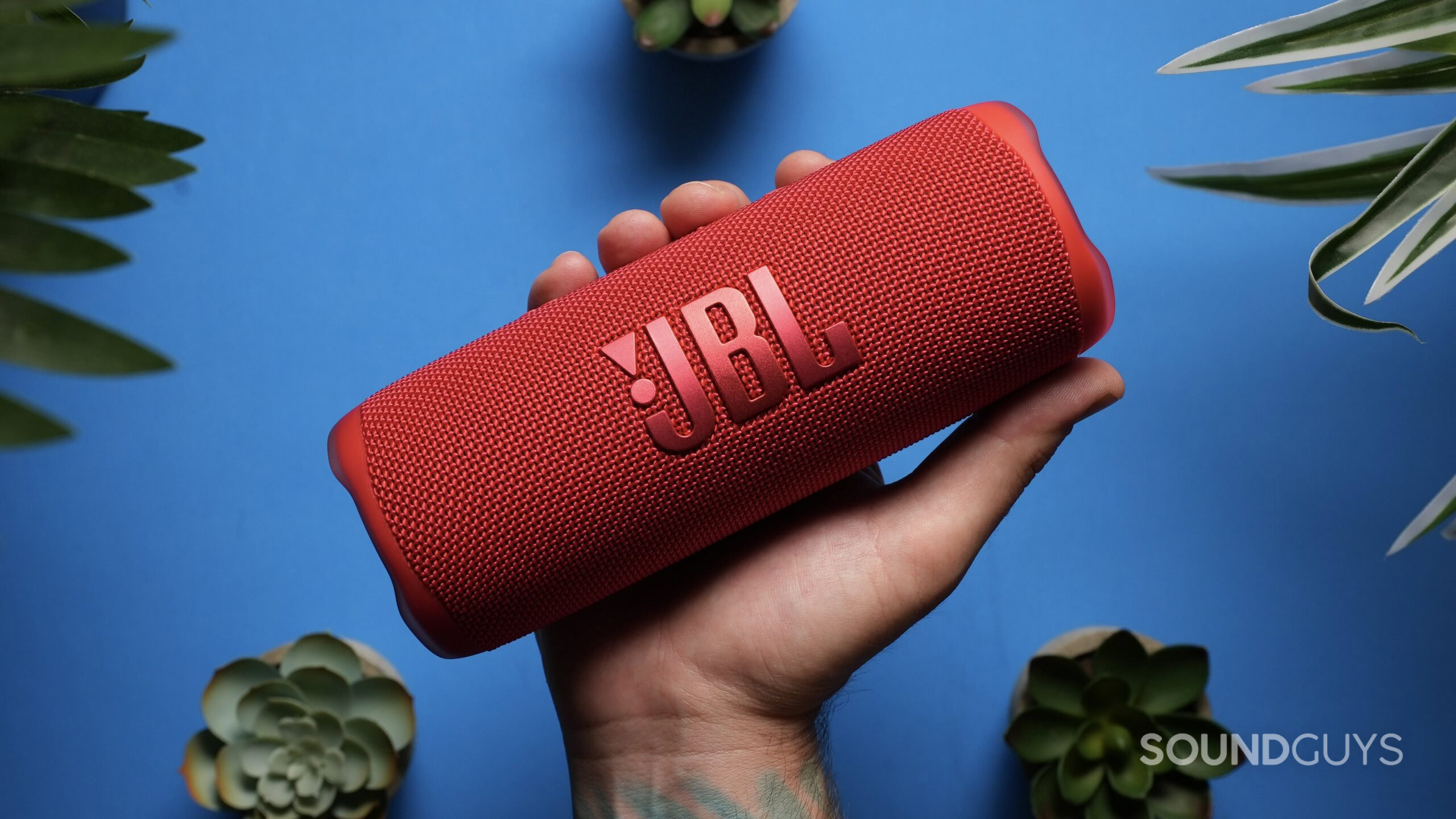 A hand holds a red JBL Flip 6.