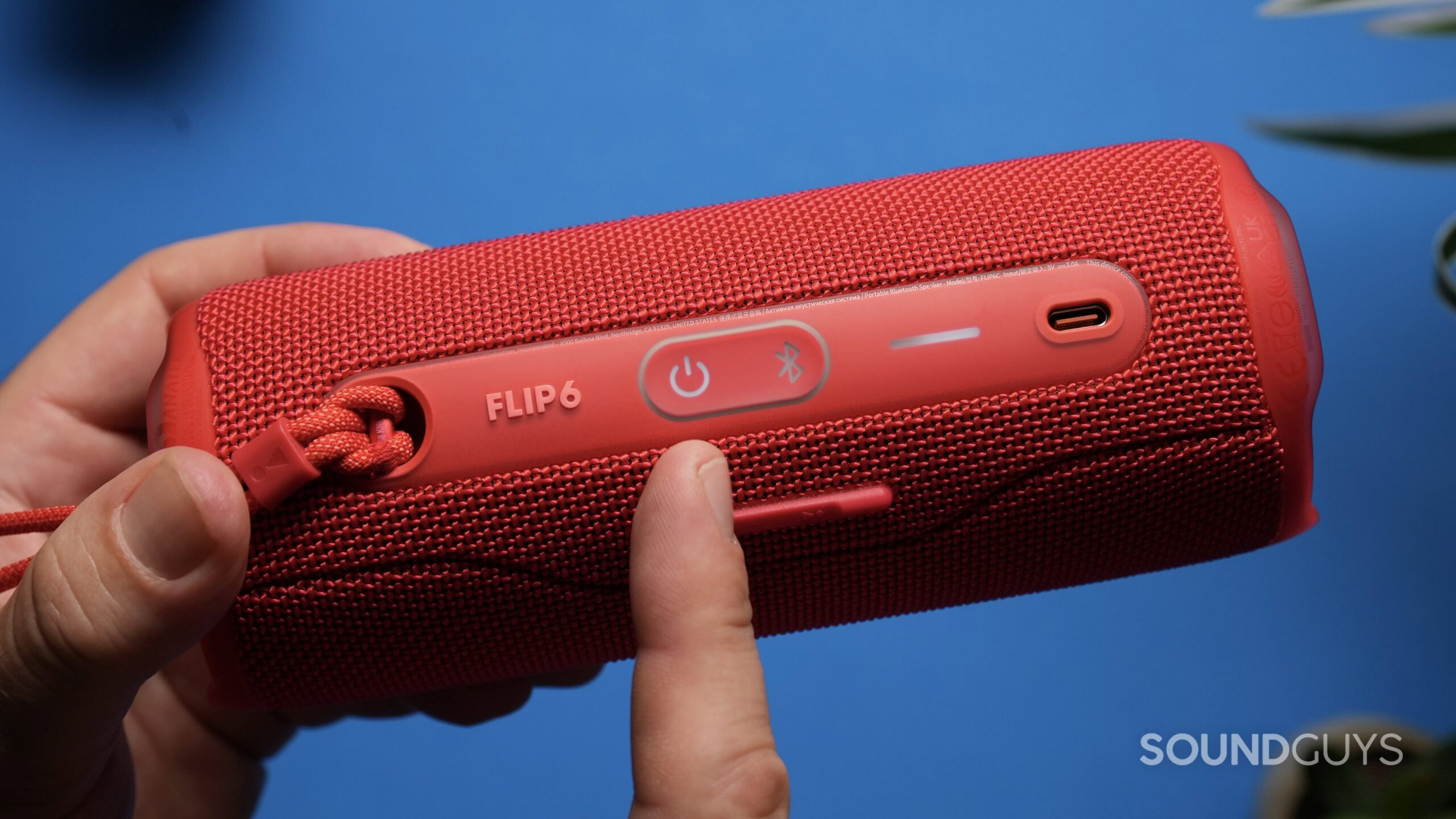 A finger points to the power button of a red JBL Flip 6