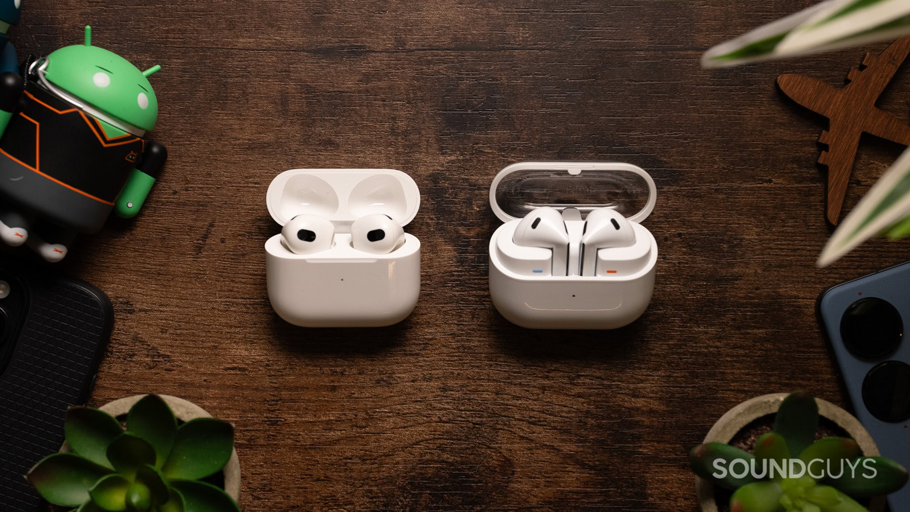 Samsung Galaxy Buds3 next to Apple AirPods (3rd generation) in case with lid open.