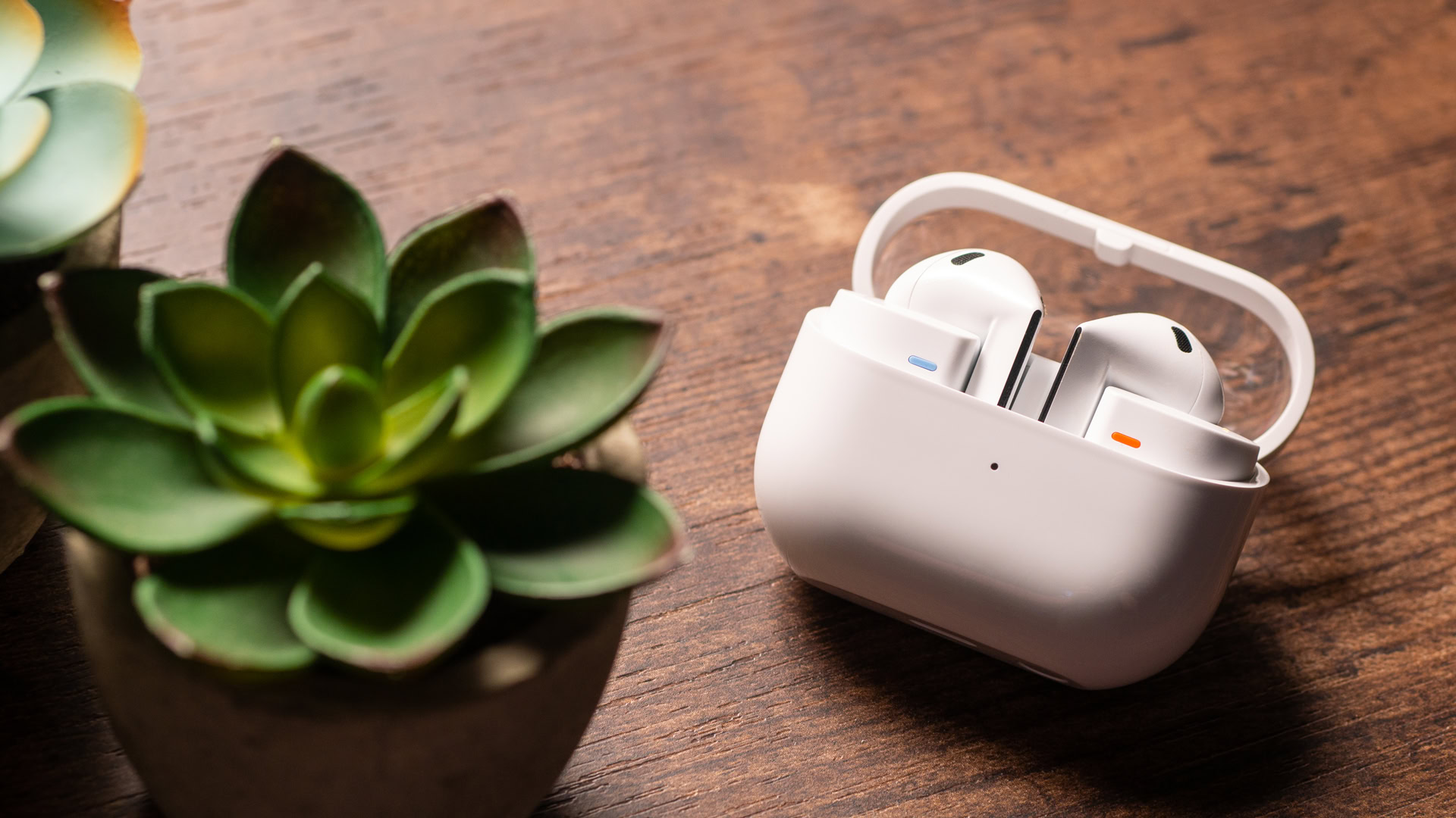 A photo of the Samsung Galaxy Buds 3 sitting in their case, atop a wooden desk.