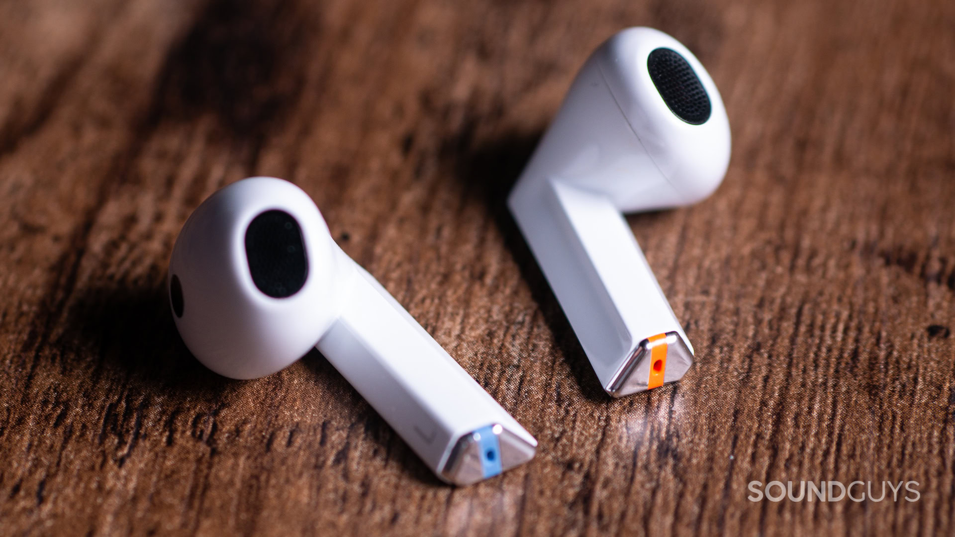 A photo of the Samsung Galaxy Buds 3 sitting on wood, with the pyramidal charging contacts showing.