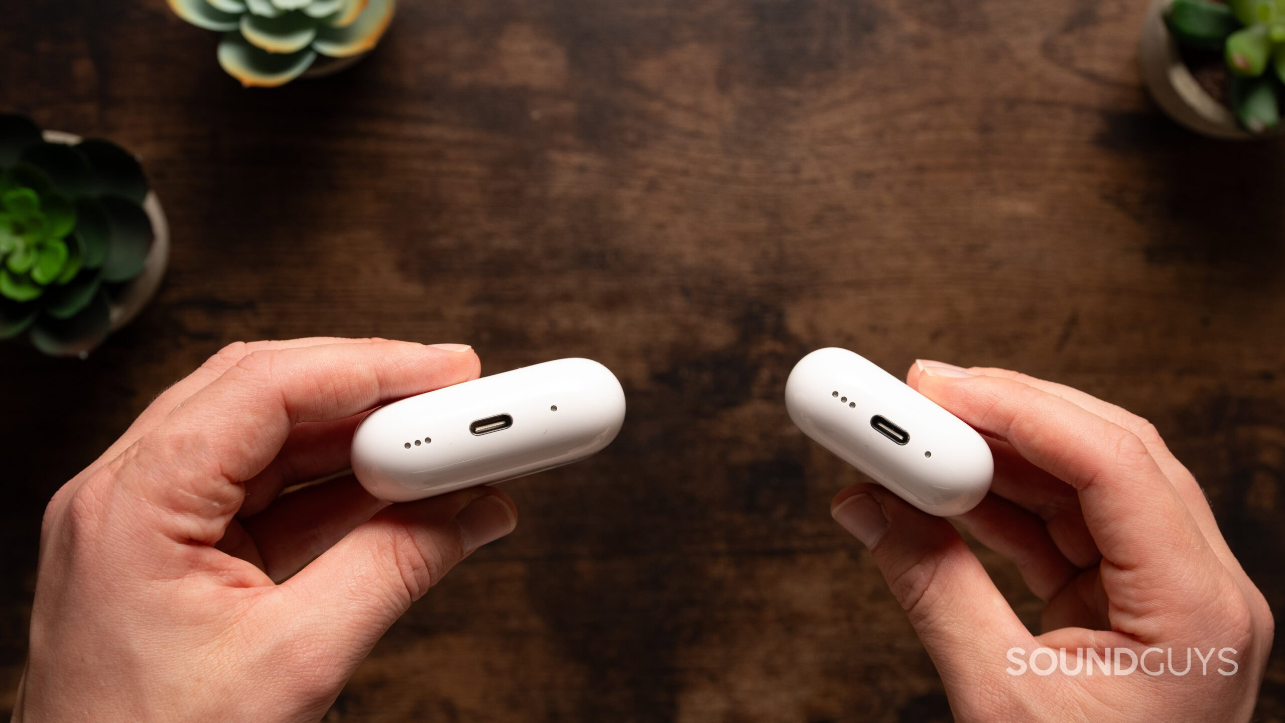 Hands holding the AirPods 4 and AirPods Pro 2 charging cases showing the USB-C port. 