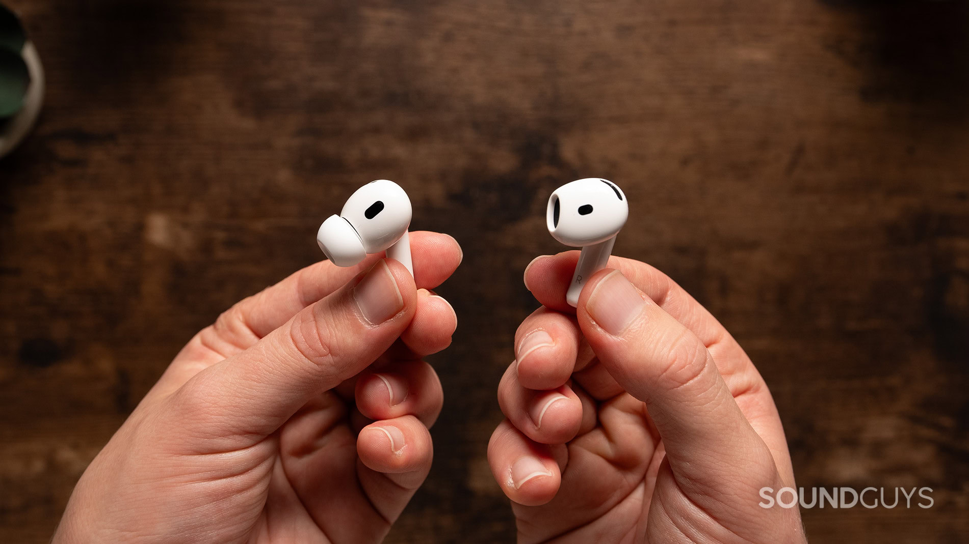 One hand holds an AirPods 4 earbud while one hand holds an AirPods Pro 2 earbud.