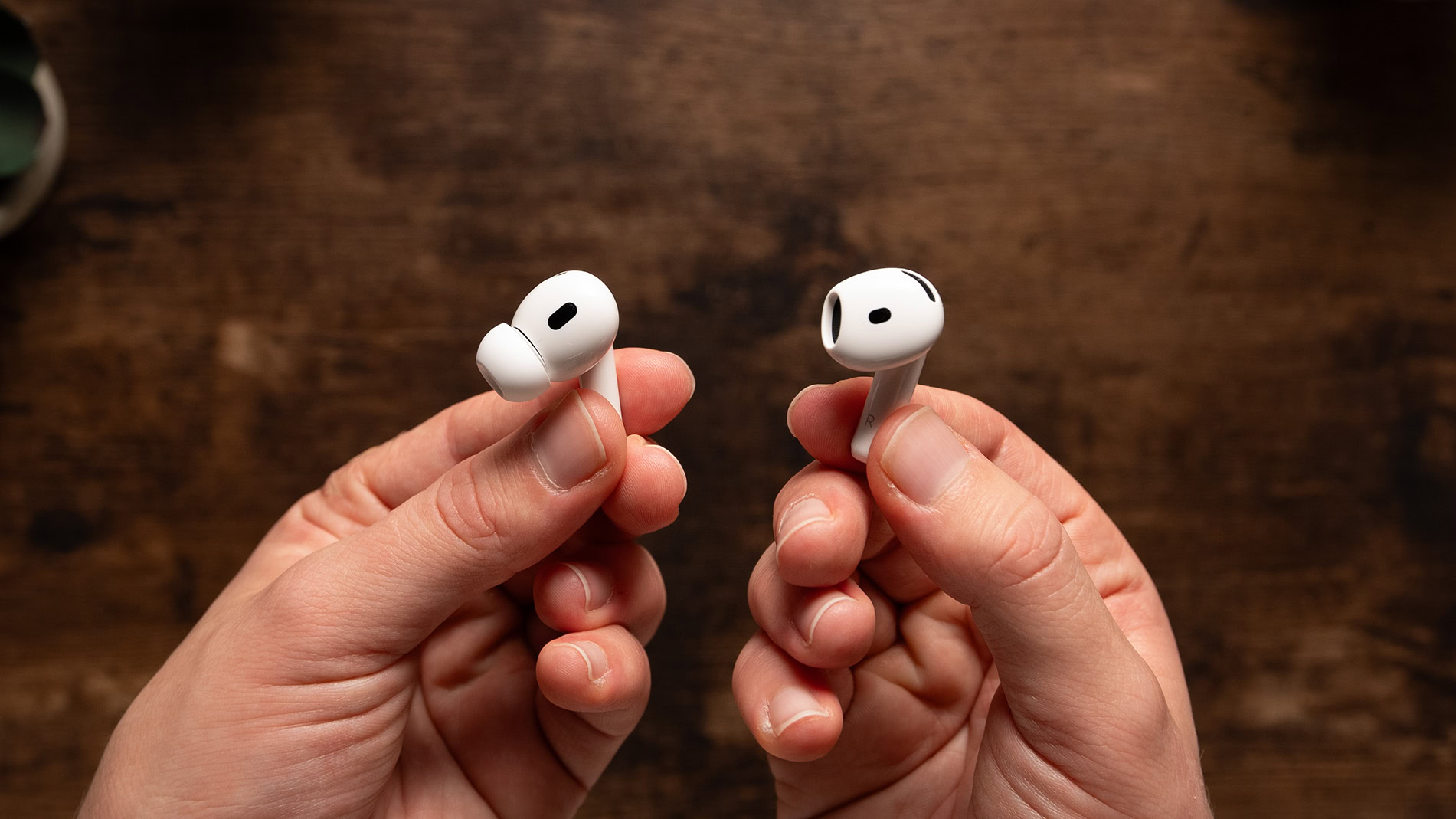 One hand holding an AirPods 4 earbud and one hand holding an AirPods Pro 2 earbud.