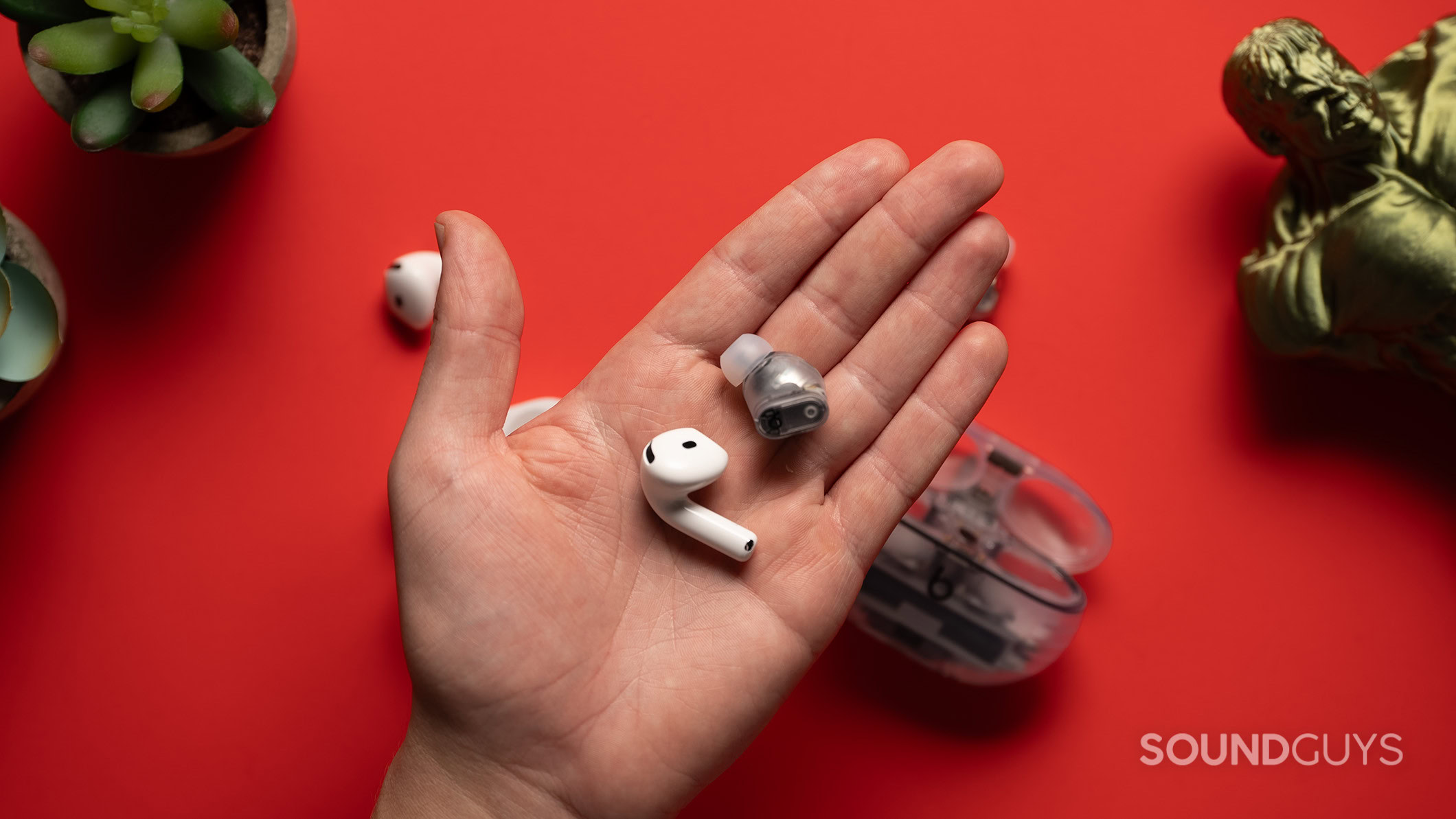 AirPods 4 and Beats Studio Buds earbuds in hand. 