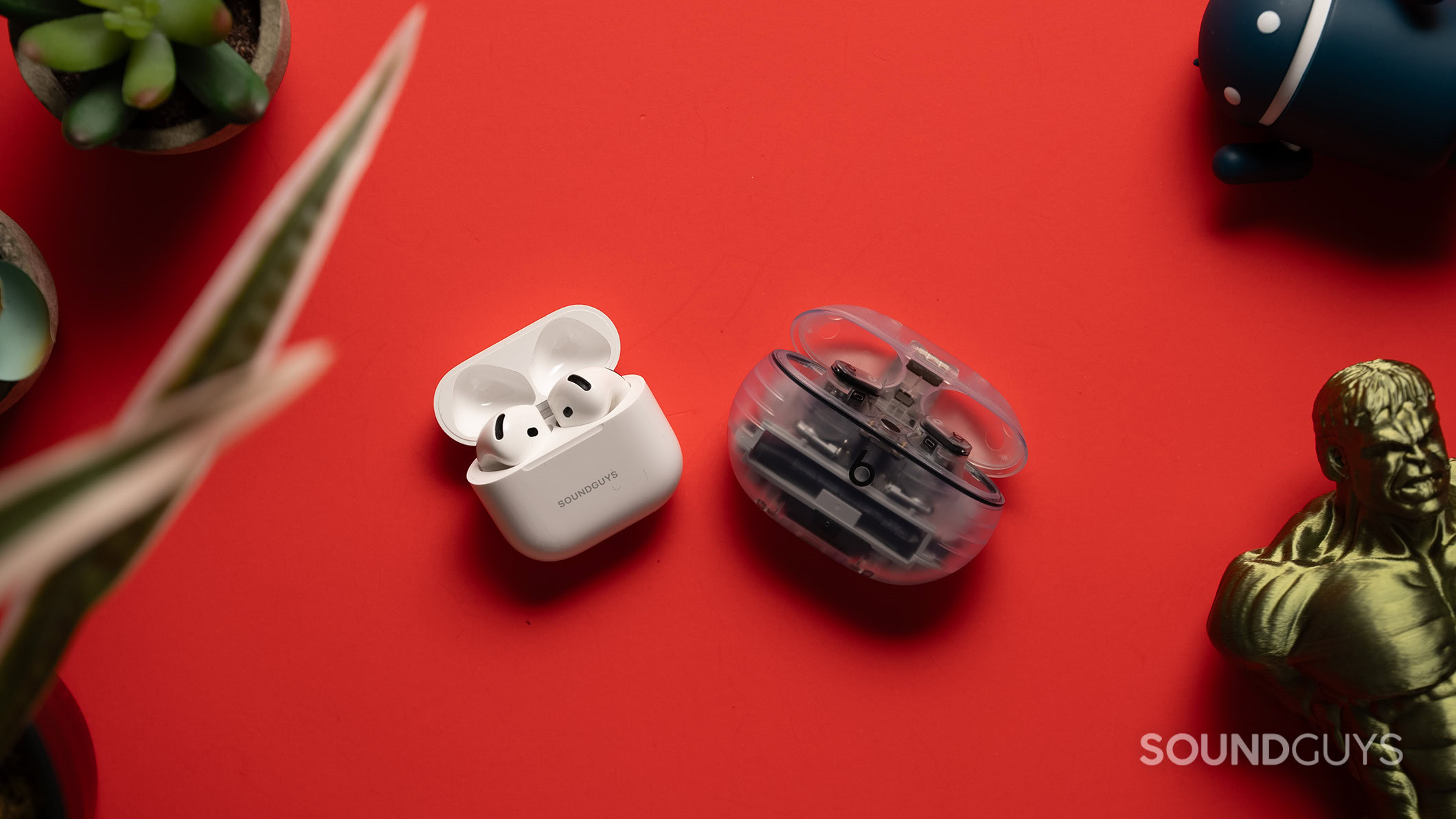 AirPods 4 next to Beats Studio Buds Plus on a table, with the earbuds inside the case.