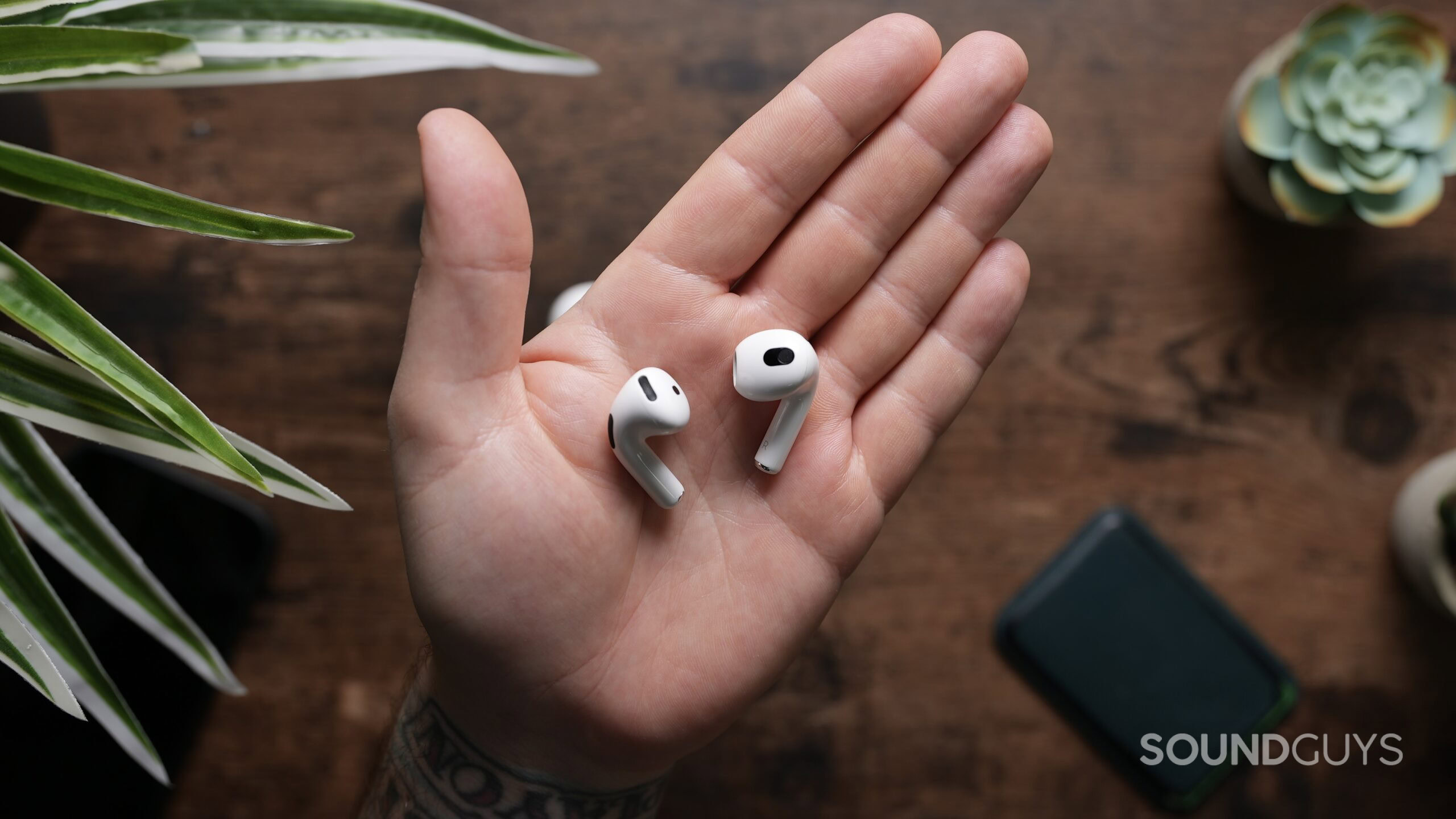 Top down shot of an Airpod 4 earbud and Airpod 3 earbud in the palm of a hand.