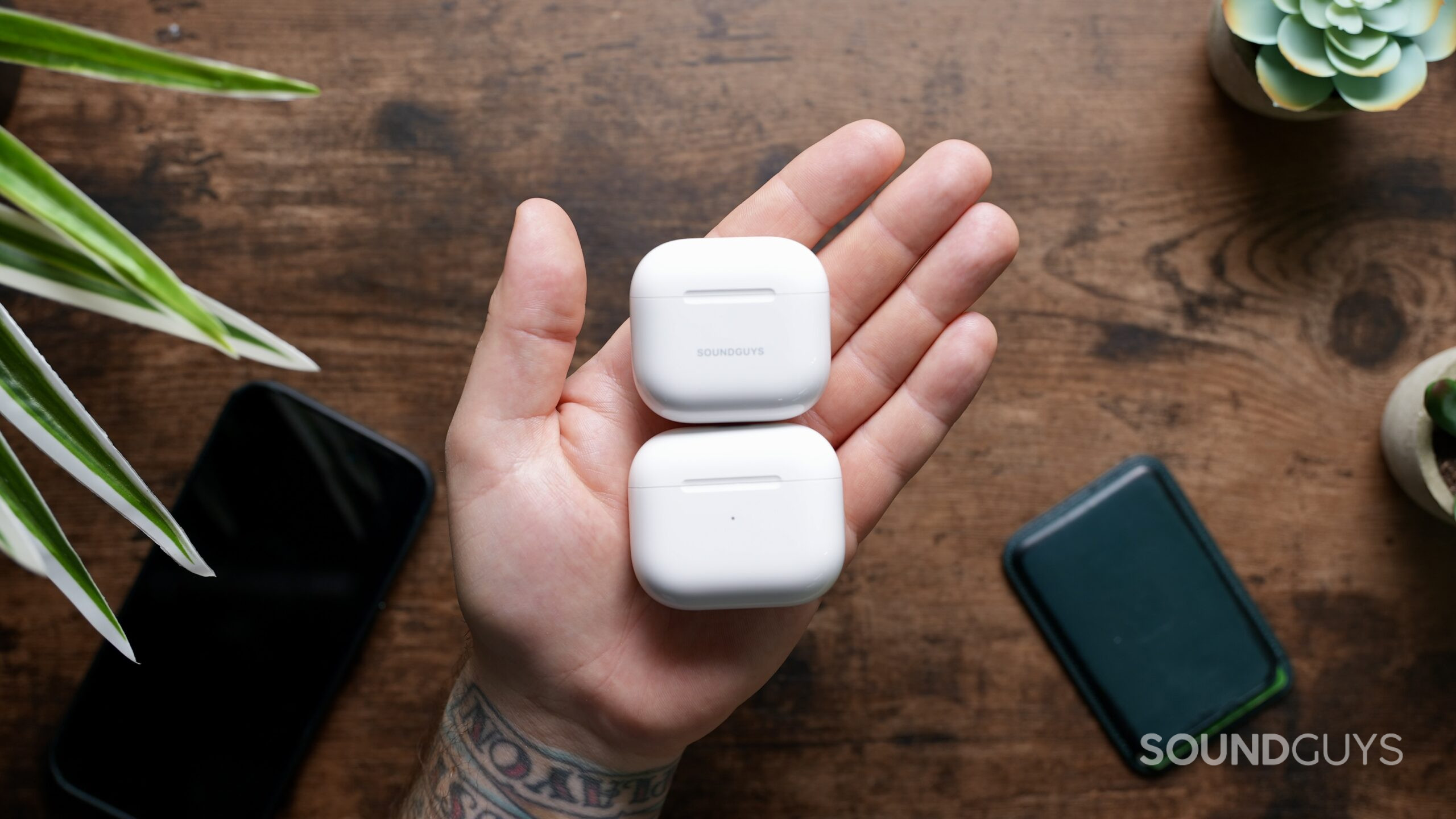 Top down photo of an AirPods 4 case and AirPods 3 case in the palm of a hand.