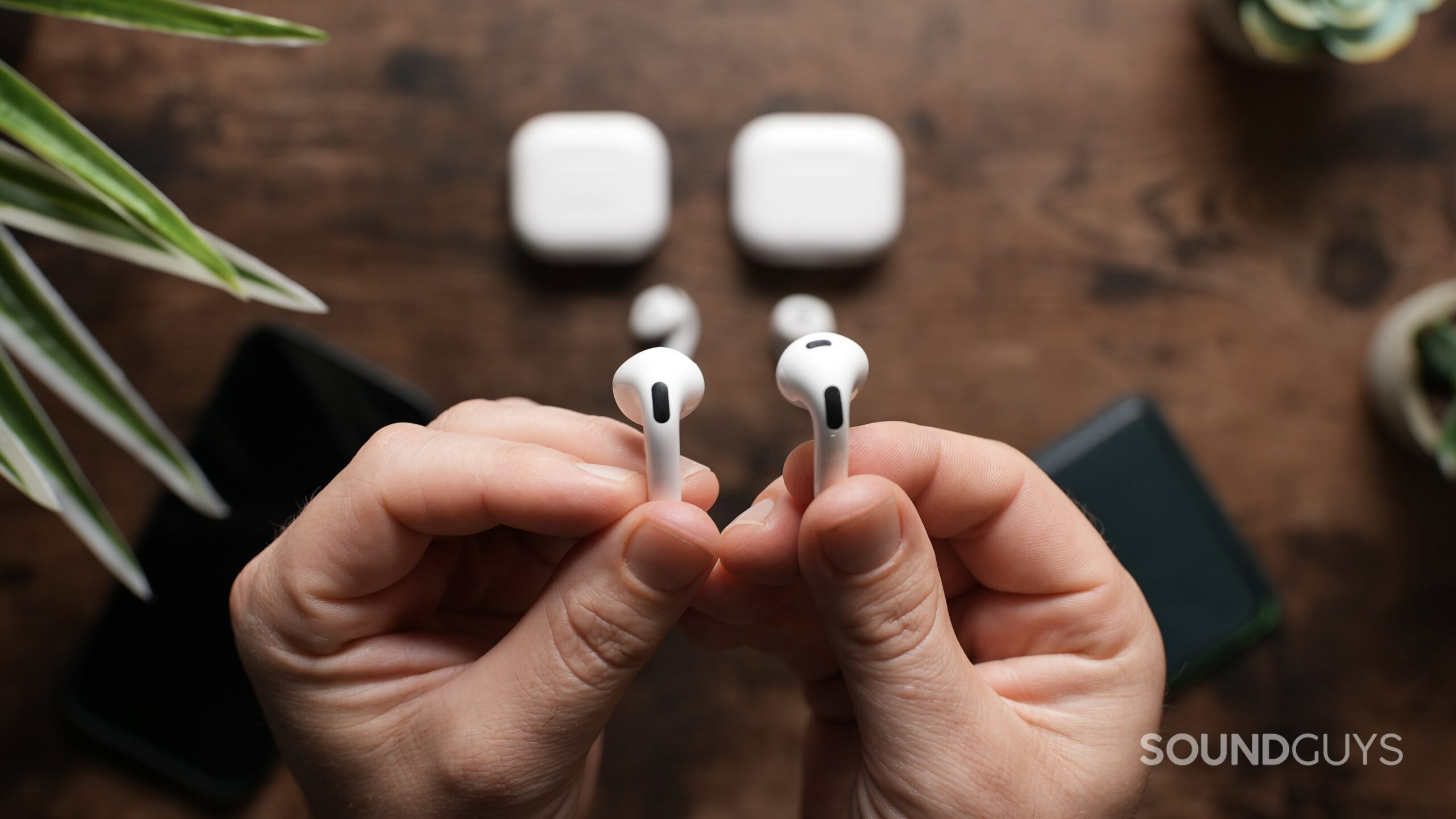 Top down view of a pair of hands, the left one holding an AirPod 4 earbud, and the right one holding an AirPods 3 earbud.