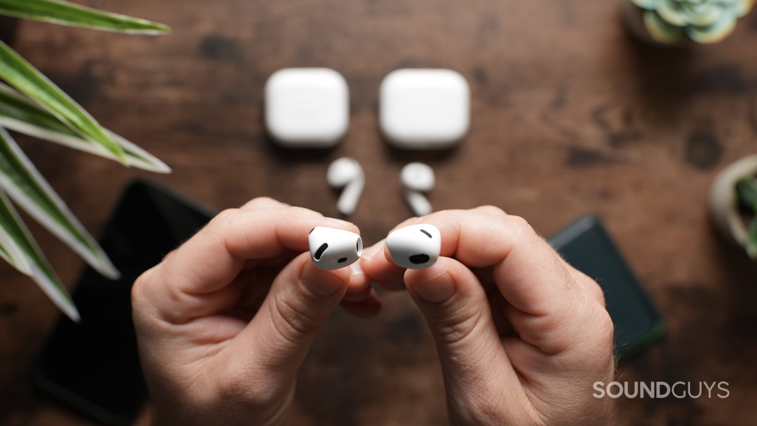 Top down view of a pair of hands, the left one holding an AirPod 4 earbud, and the right one holding an AirPods 3 earbud.