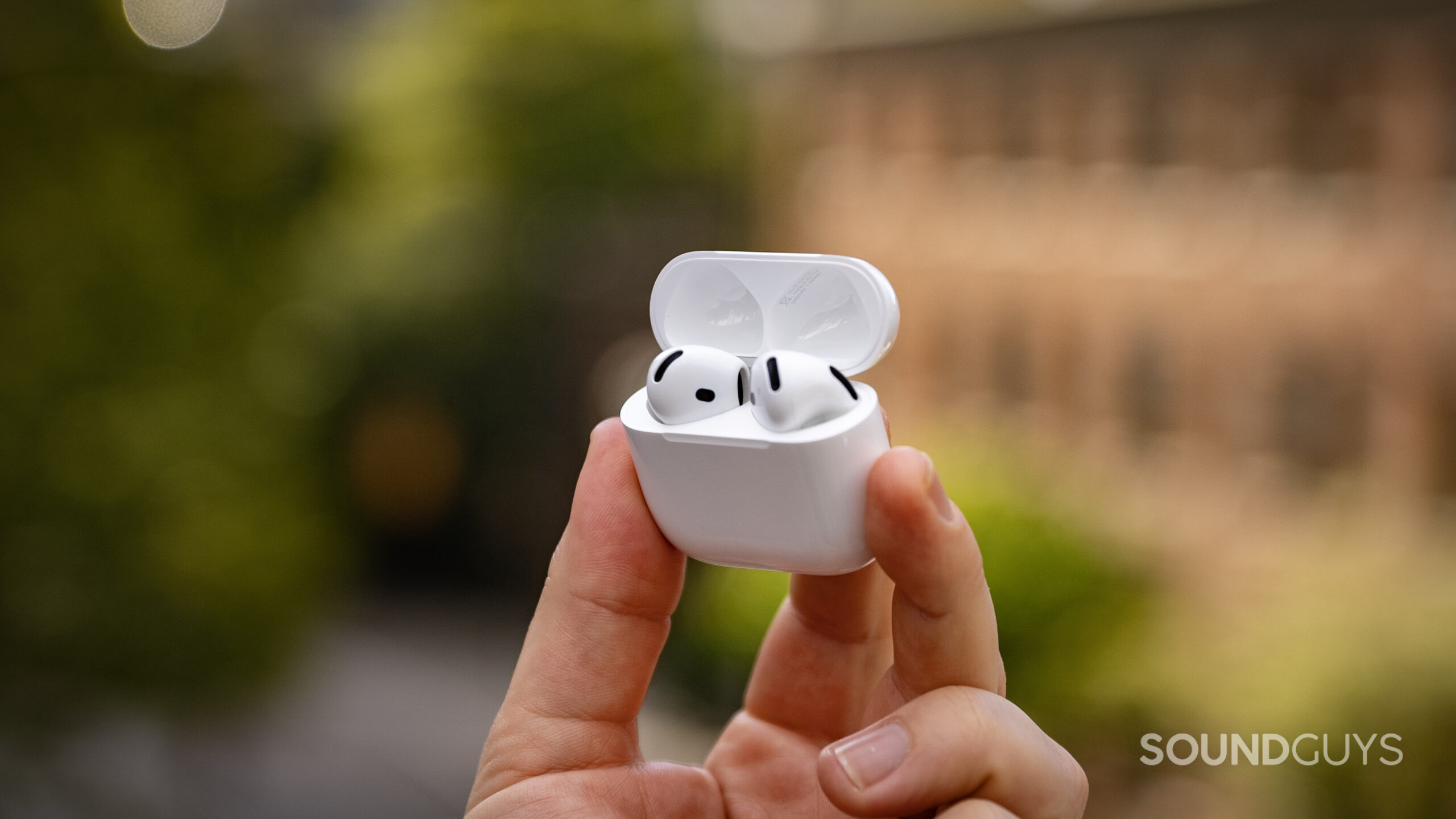 A hand holds the AirPods 4 earbuds inside their charging case. 