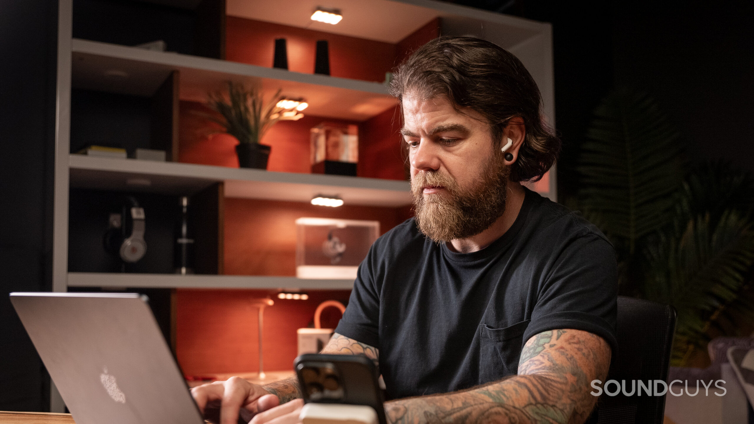 A man at a desk looks at a computer while wearing AirPods 4. 