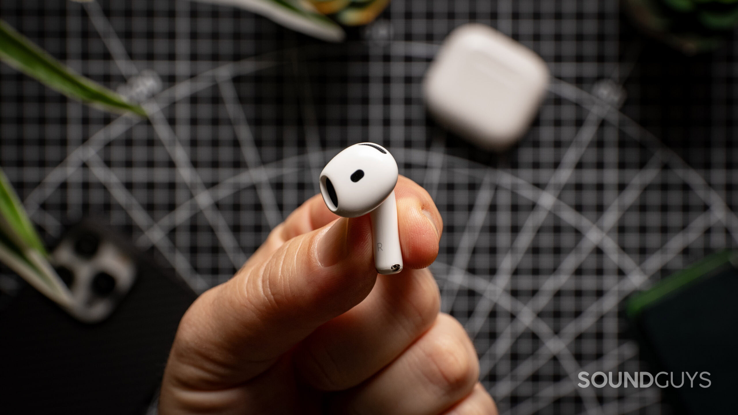 A hand holds the AirPods 4 earbud over a table.