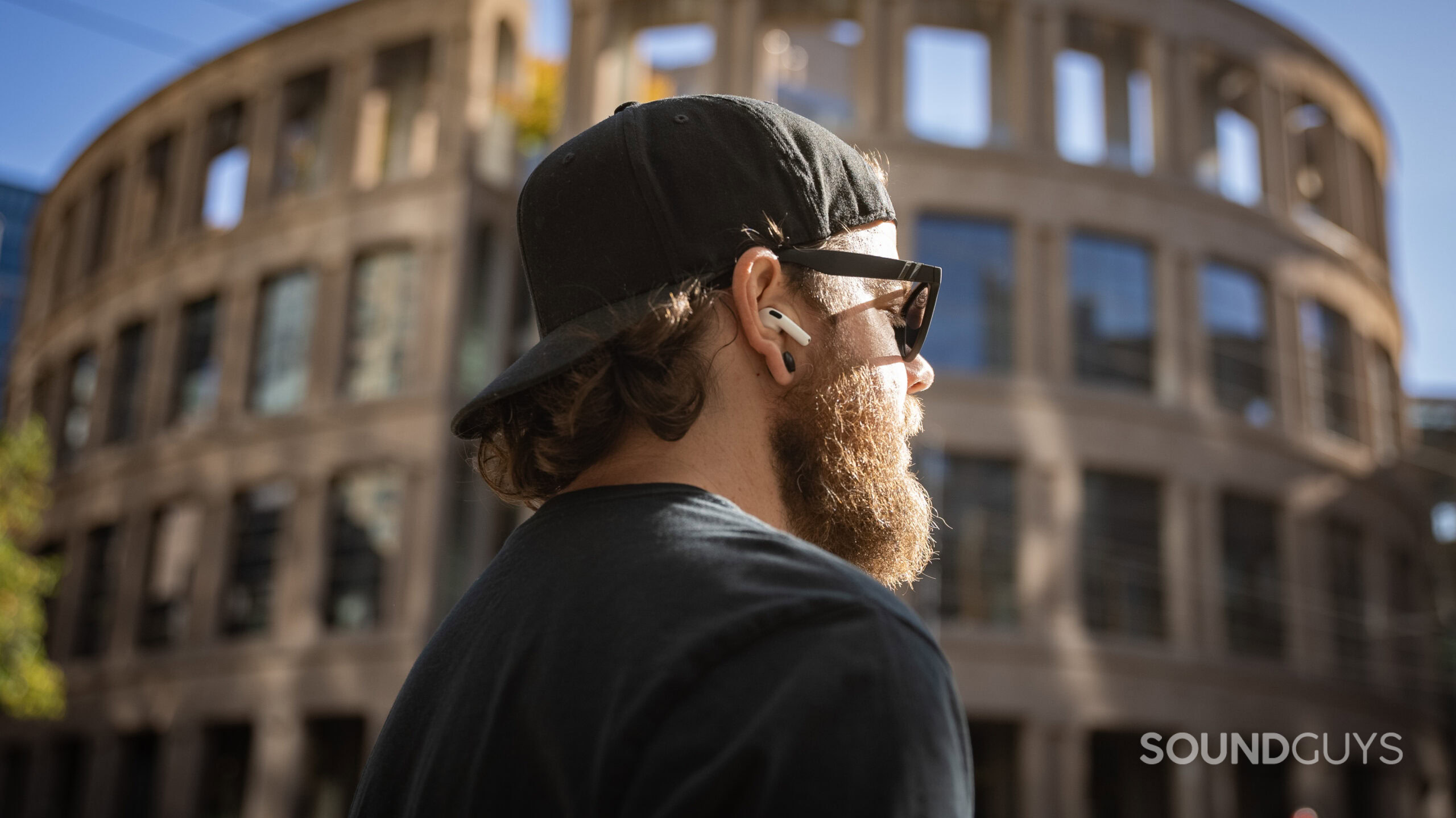 A man wears the AirPods 4 with Active Noise Cancellation outdoors in front of a large building. 