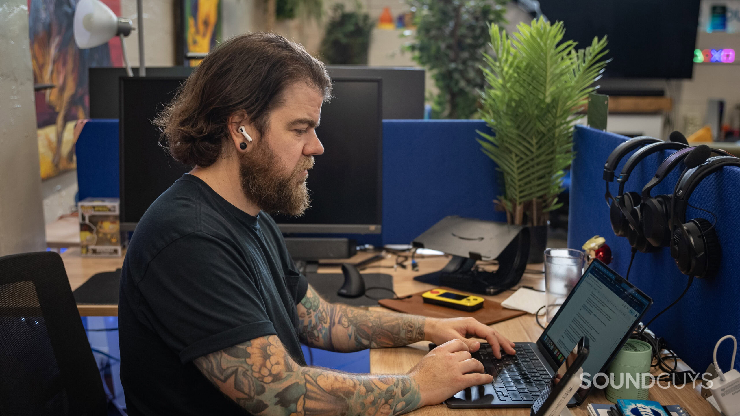 A man wears an Apple AirPods 4 with Active Noise Cancellation earbud while working at a desk. 