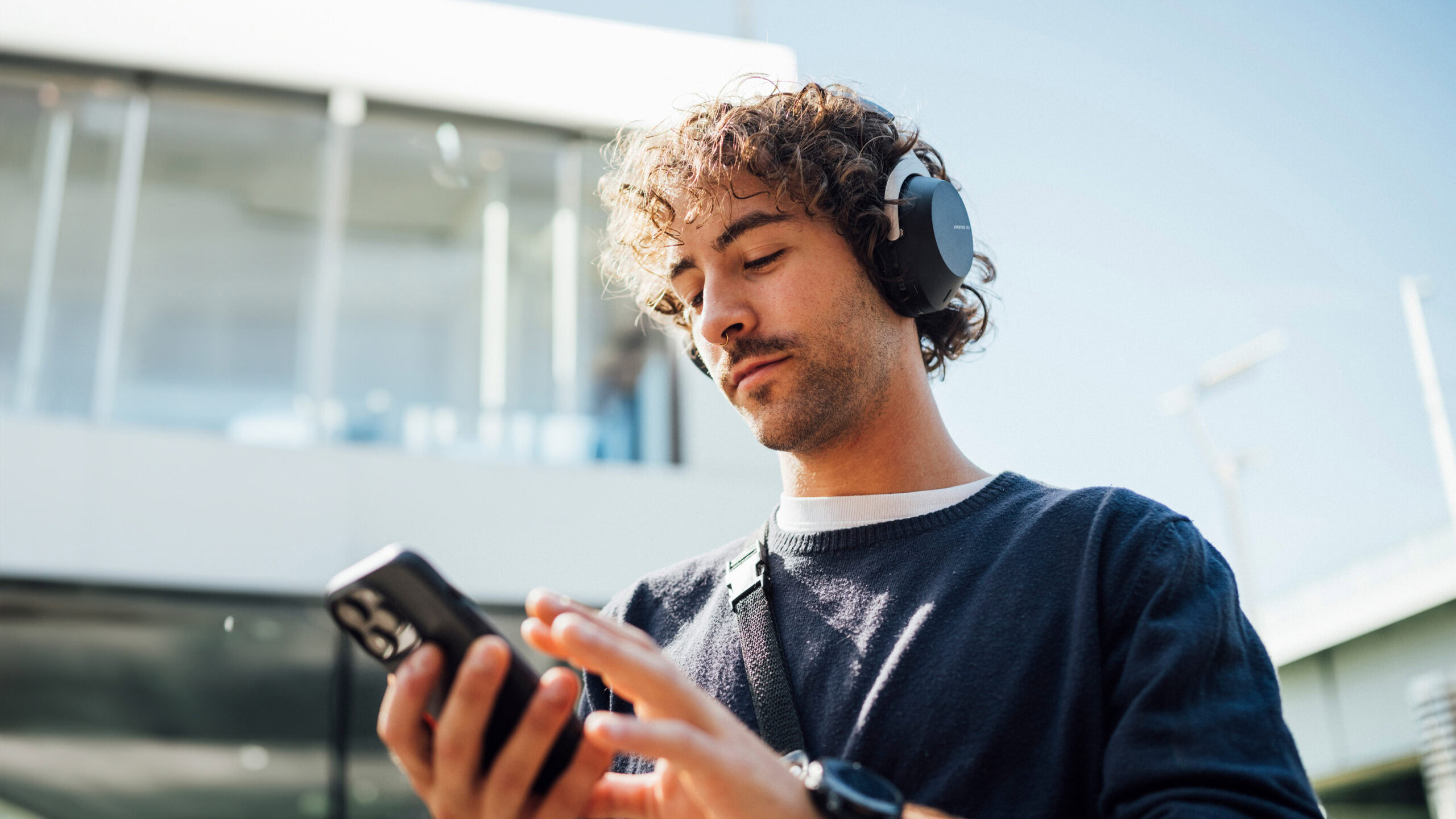 A man wears the Beyerdynamic AVENTHO 300 headphones while looking at a phone.