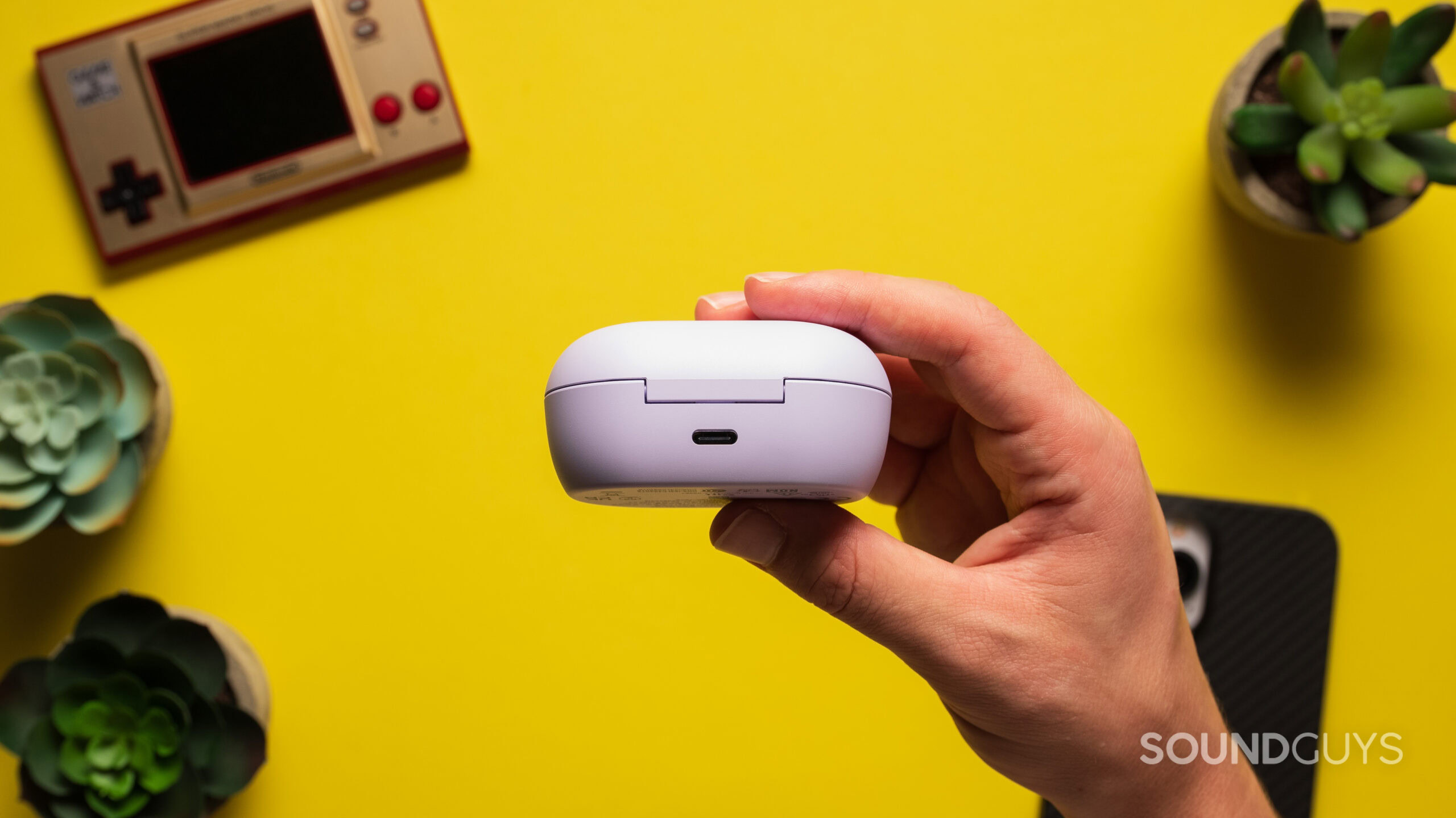 A hand holds the Bose QuietComfort Earbuds charging case showing the USB-C charging port.