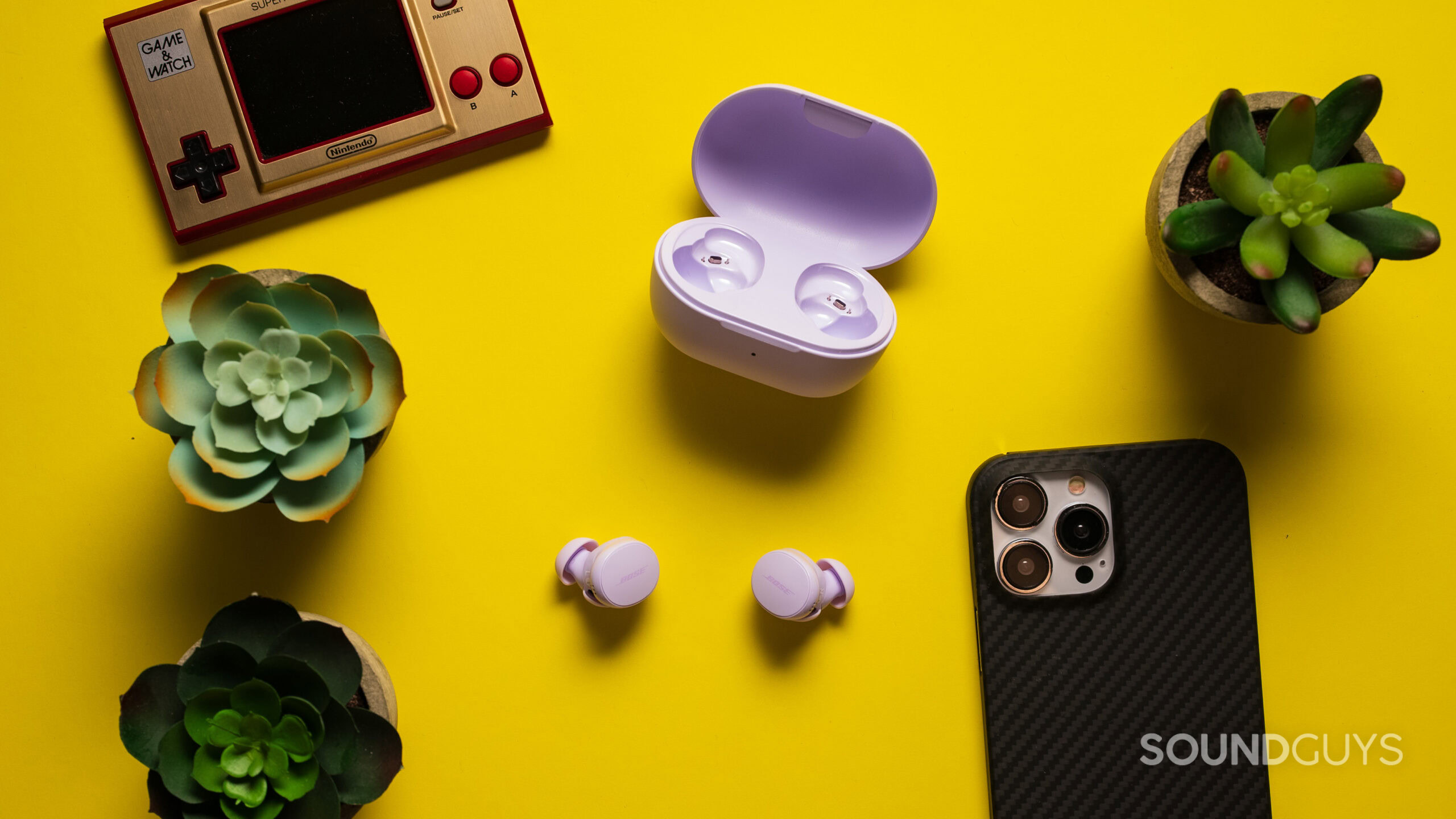 Bose QuietComfort Earbuds next to the case on a table with a phone and plants.