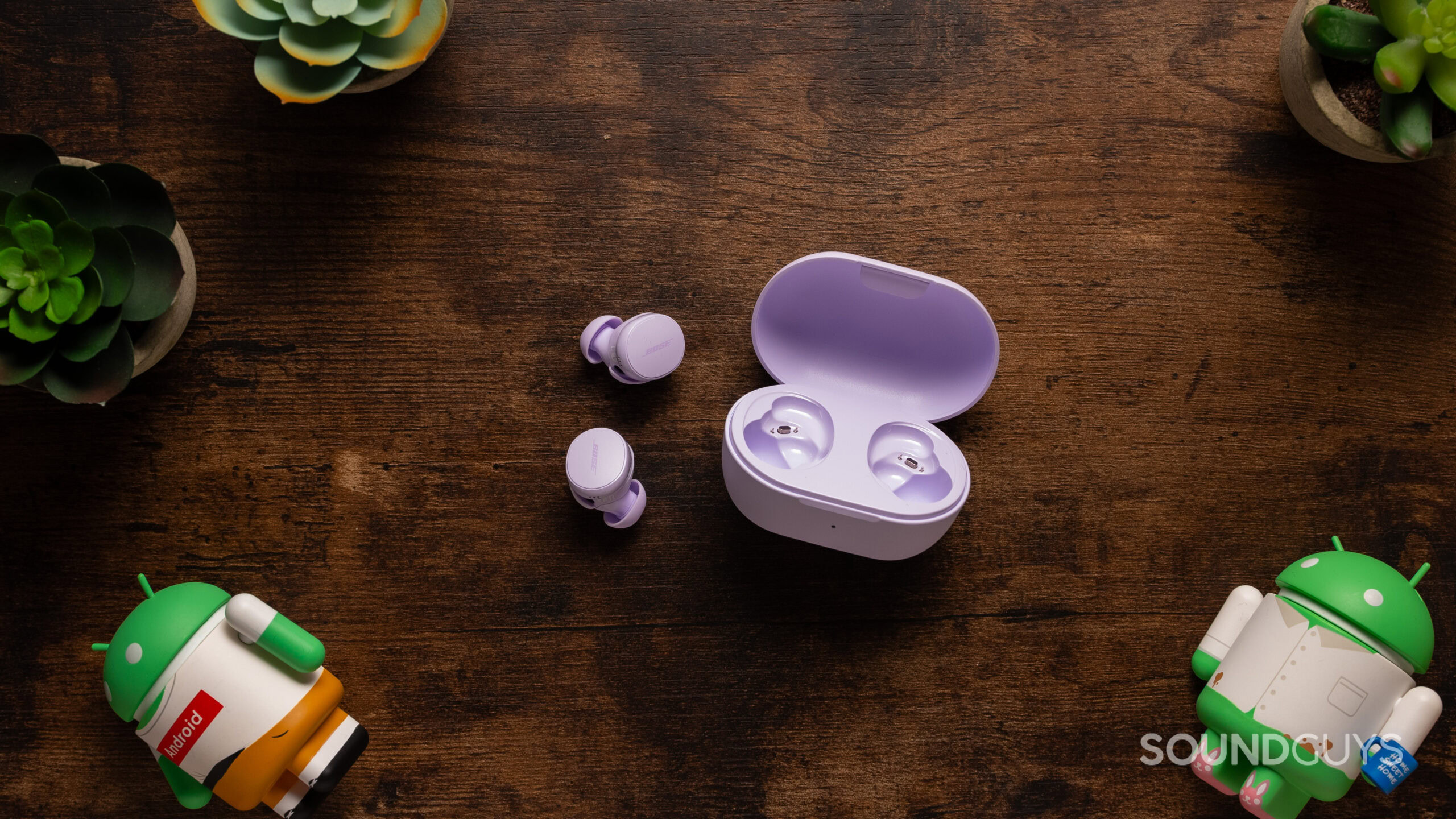 Bose QuietComfort Earbuds next to their case on a wood table. 