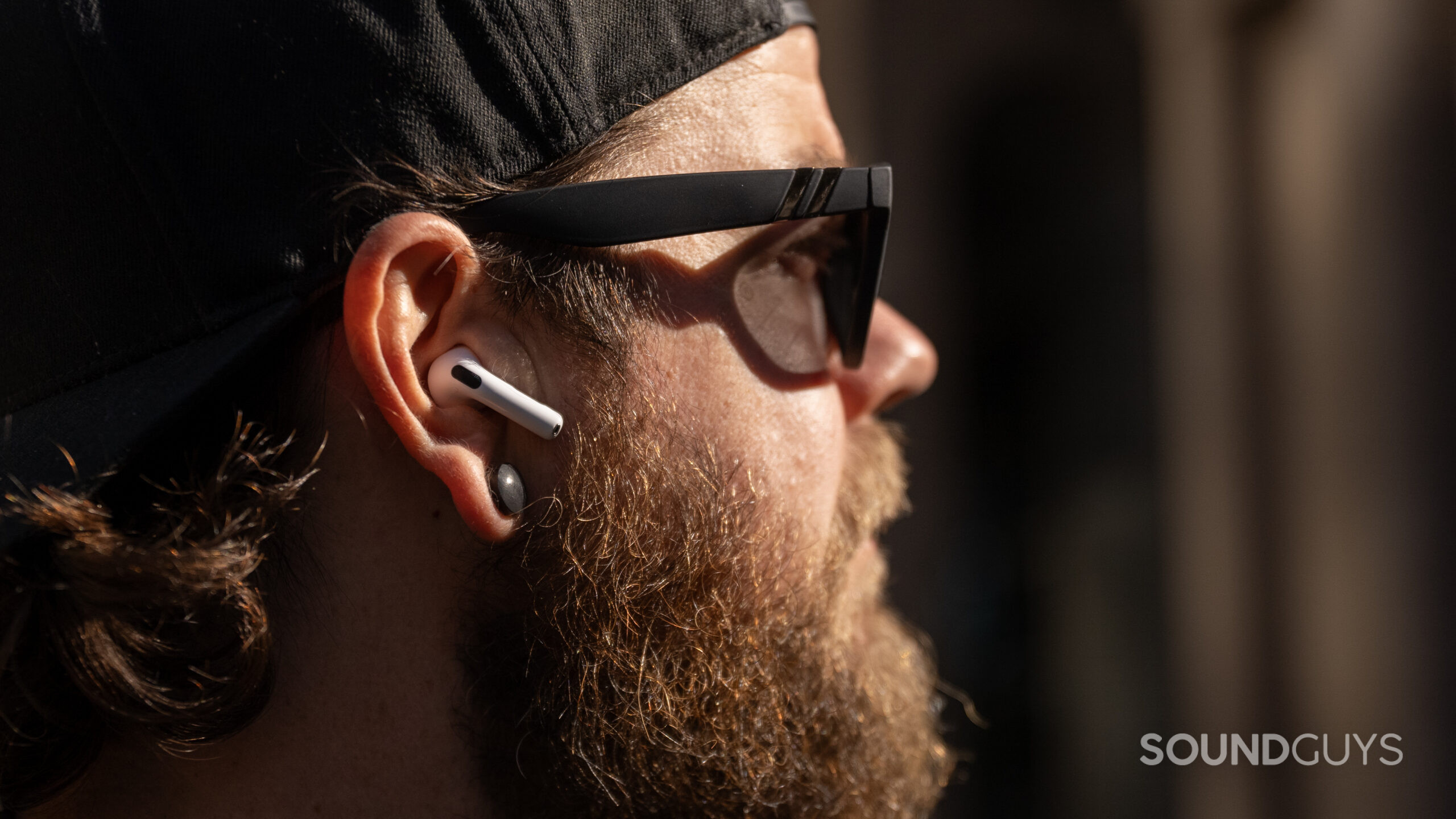 A close-up photo of a sunglasses-wearing man with beard and AirPods 4.