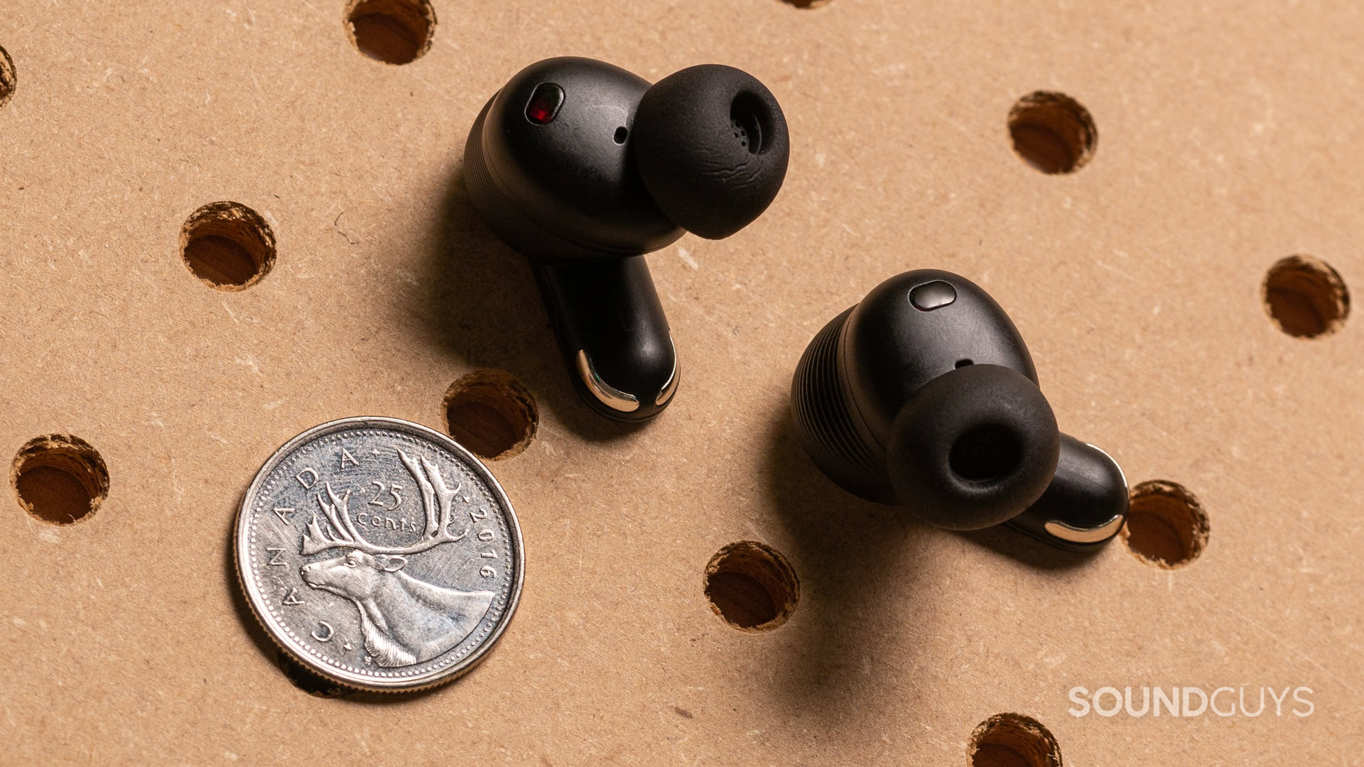 A photo of the JBL Tour Pro 3's earbuds, next to a quarter.