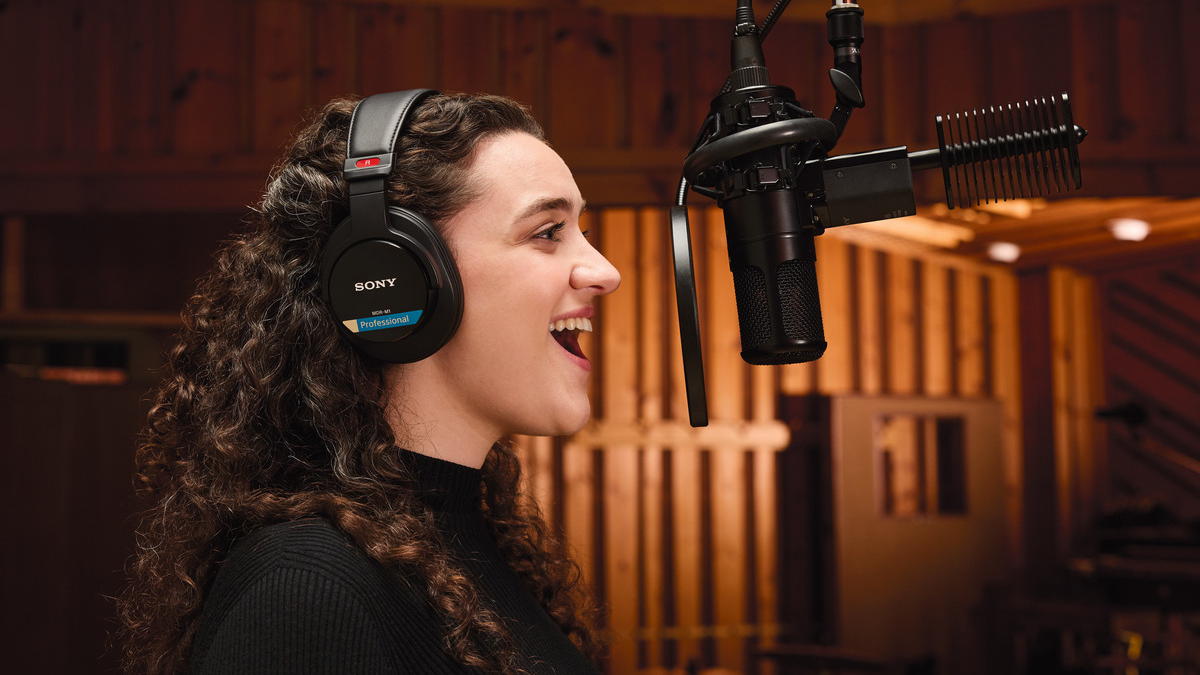 a woman wearing the sony mdr-m1 in a recording studio, singing into a microphone