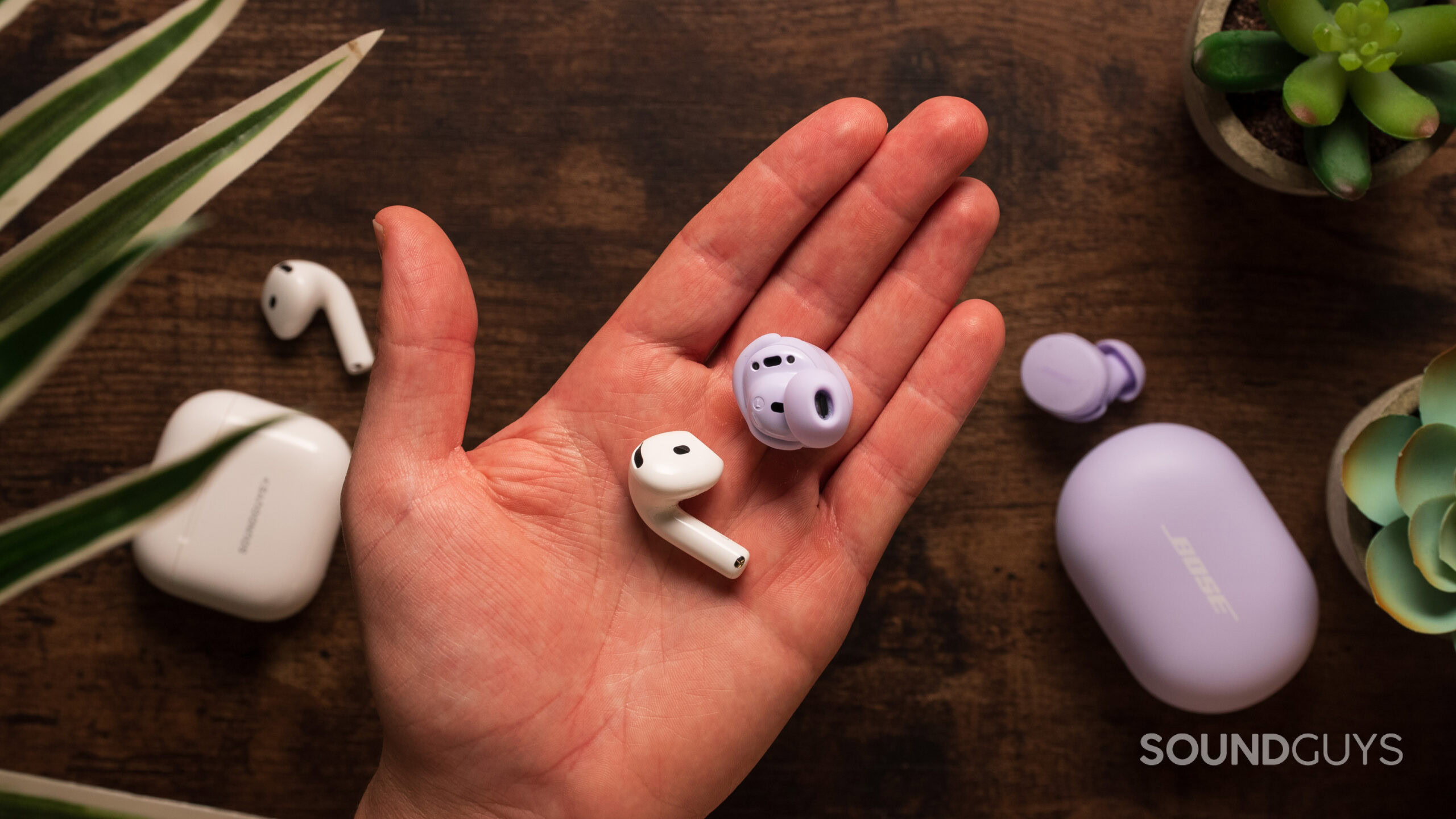 A hand holds a AirPods 4 earbud and a Bose QuietComfort earbud.