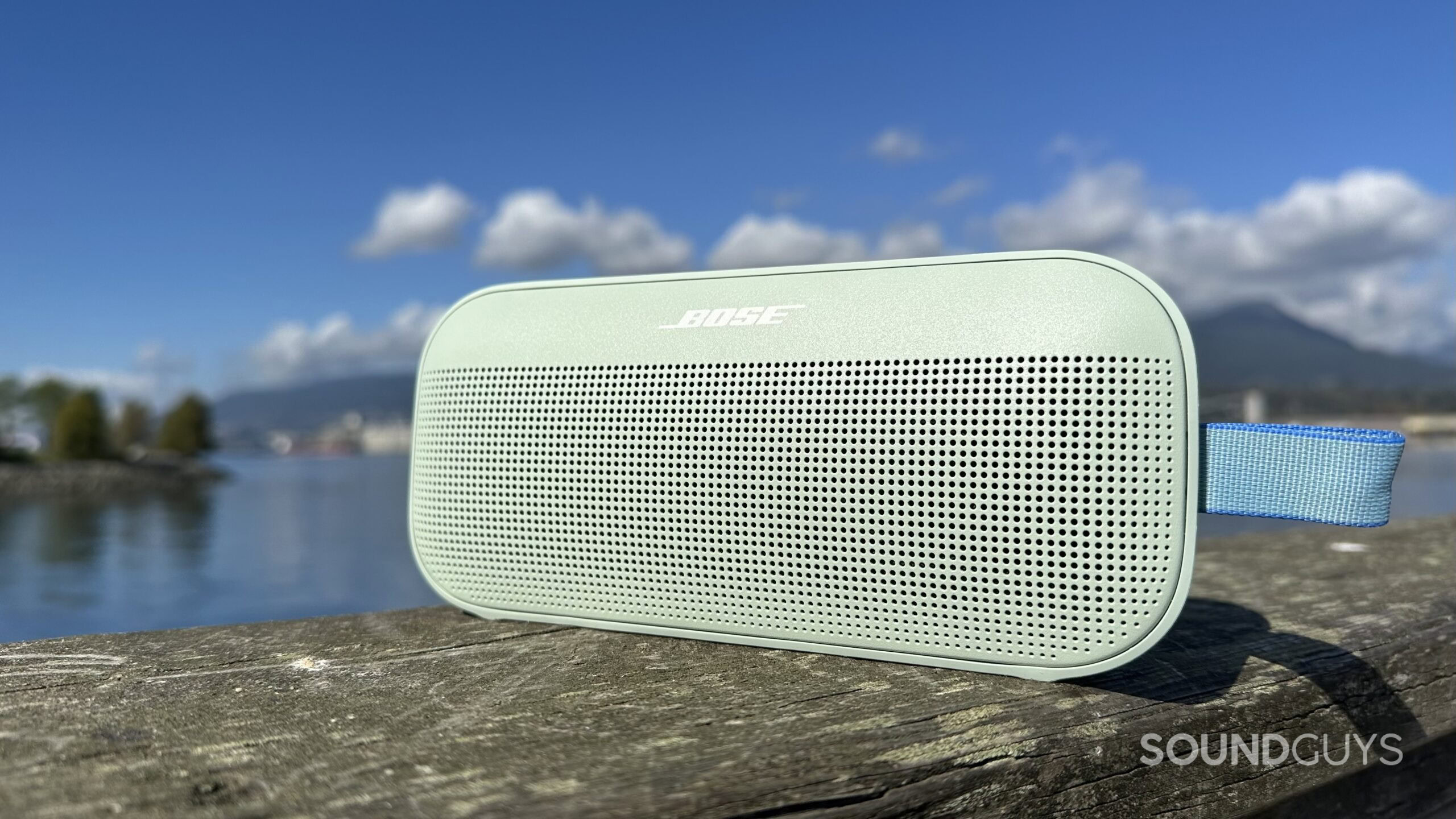 A Bose SoundLink Flex 2nd Gen on a pier with water and mountains in the background.